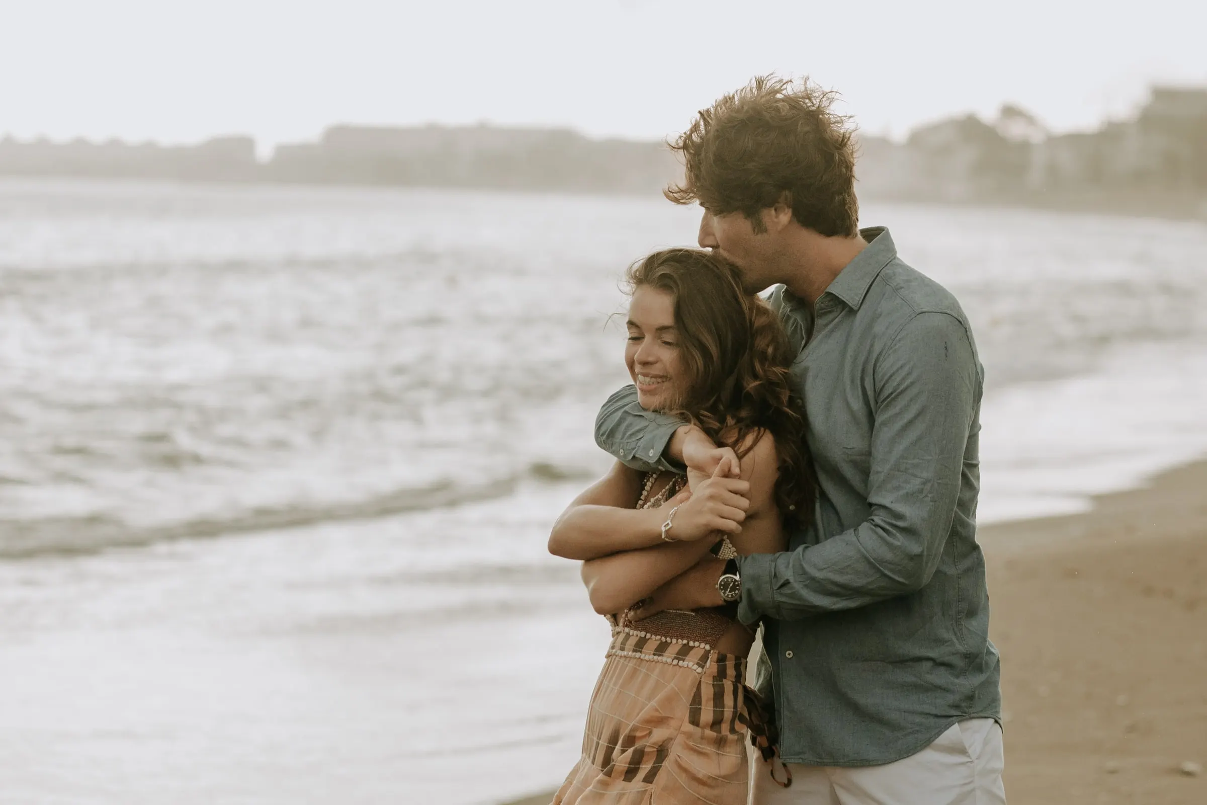 Arnaud abraza a Lauren por detrás y le besa la cabeza junto al mar, sesión preboda en la playa de Sotogrande