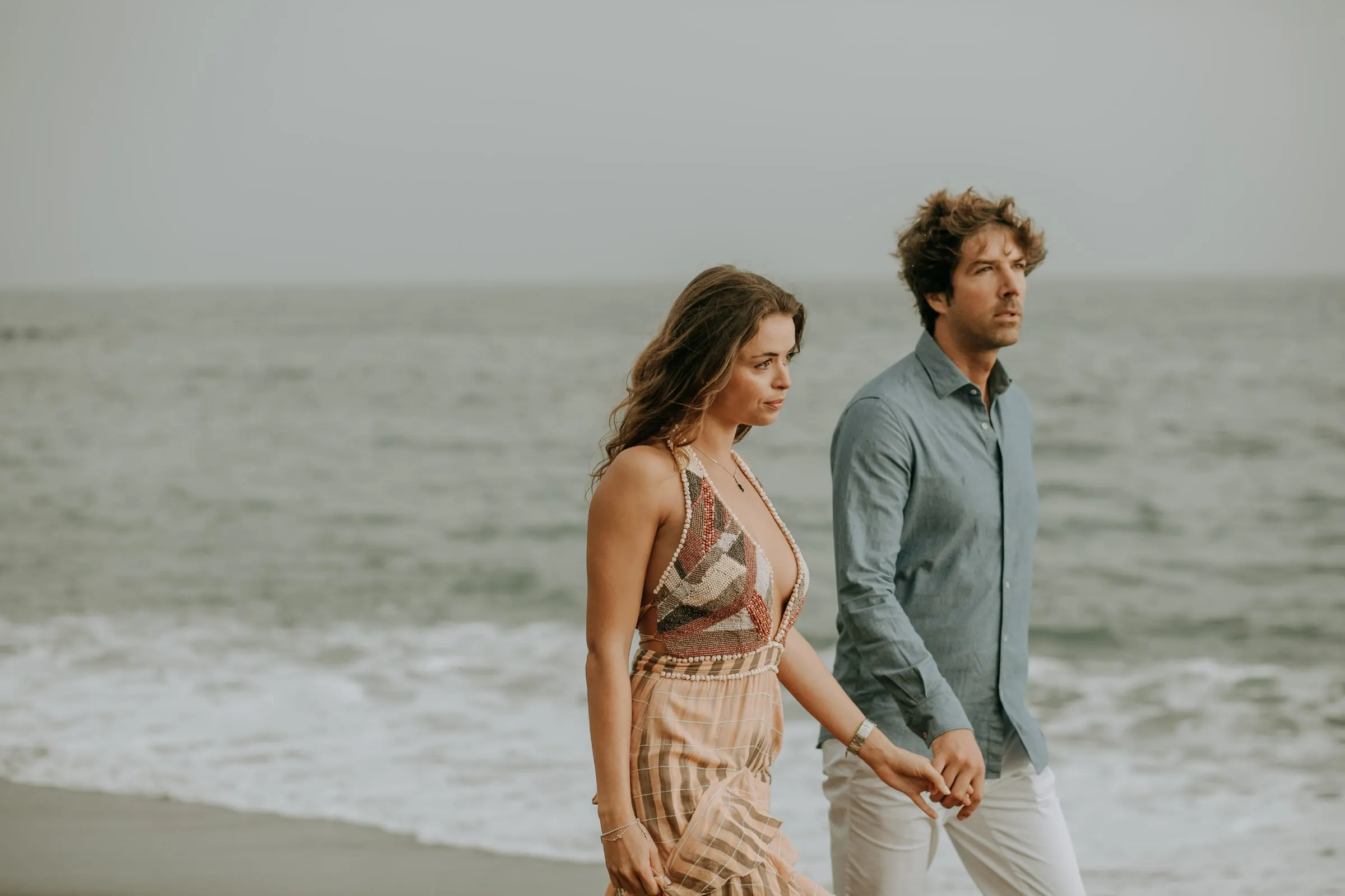 La pareja camina de la mano entre las olas, mirando al mar, sesión preboda en la playa de Sotogrande