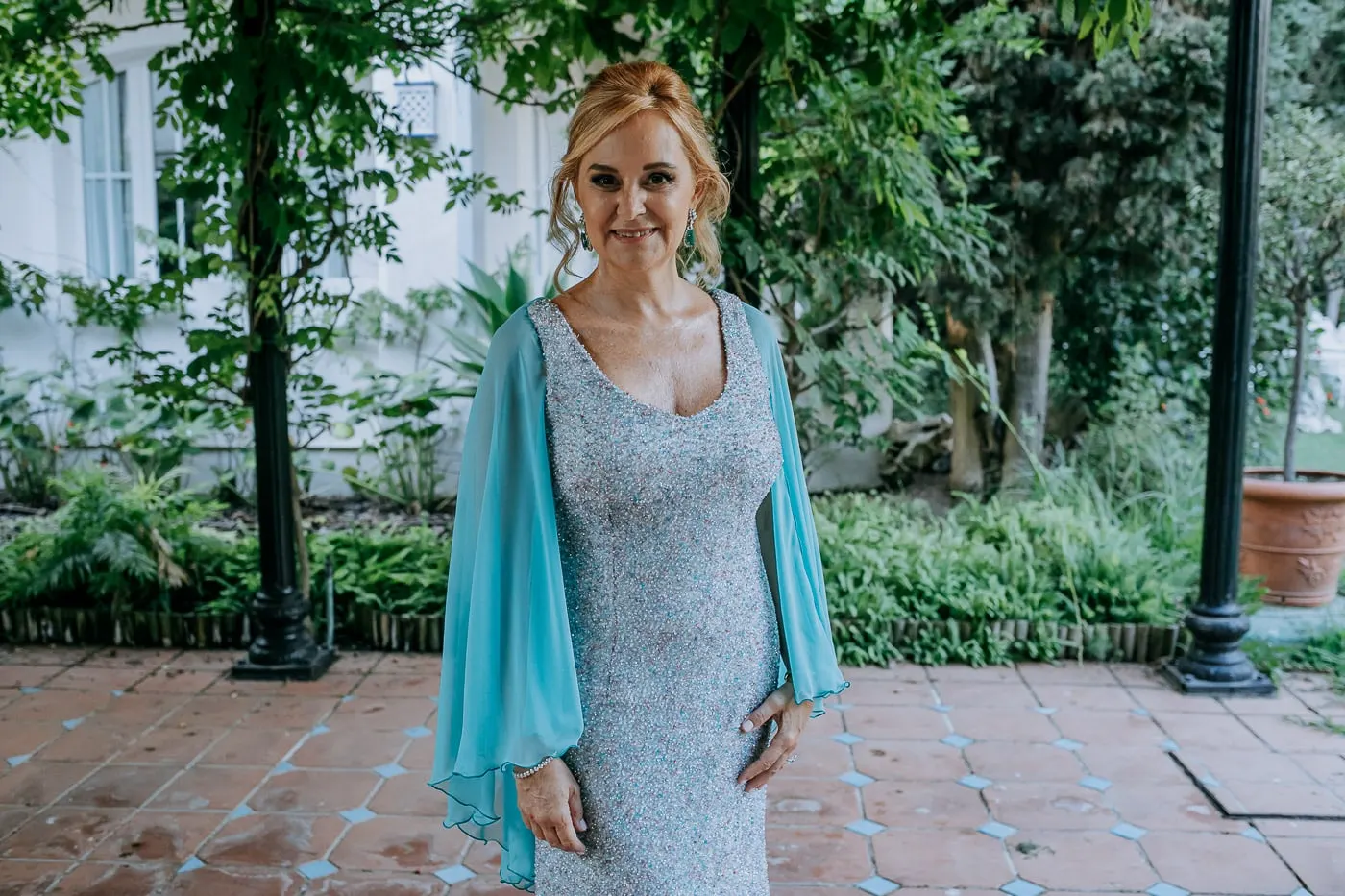 La novia sonríe bajo la pérgola, con la capa sobre los hombros