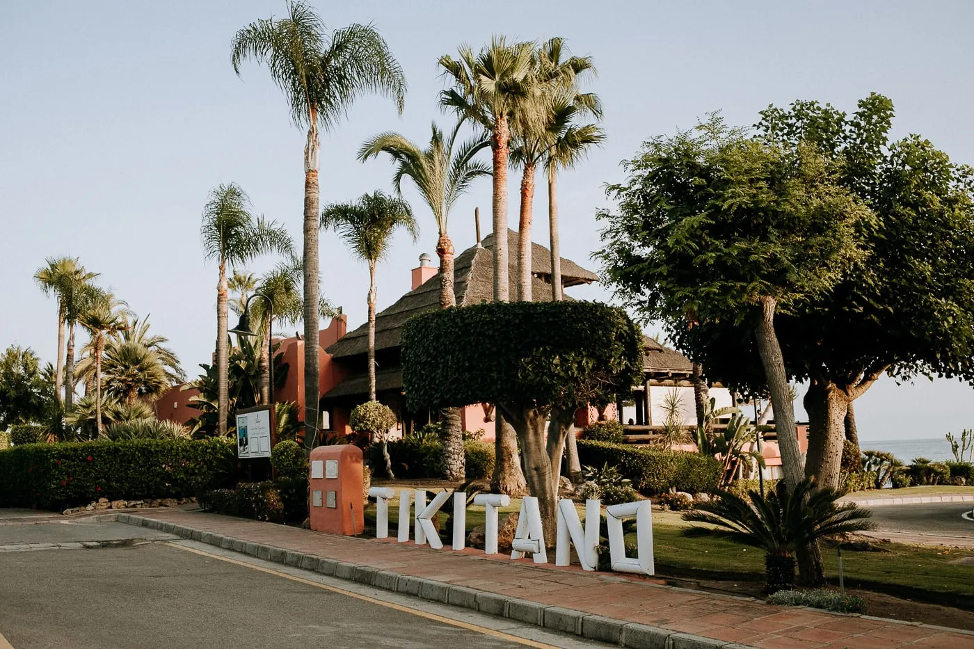 El letrero de Tikitano junto al camino, con el tejado de paja y las palmeras, Estepona
