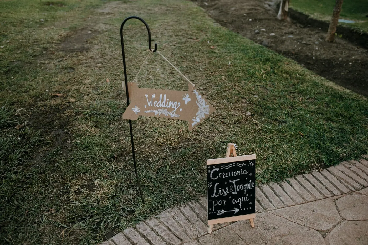 Cartel de boda y pizarra que señalan el camino a la ceremonia en el césped