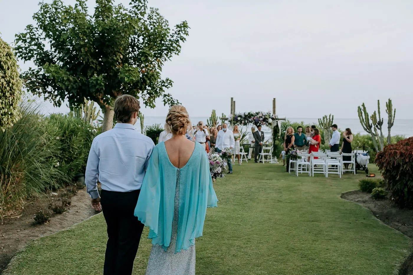 La novia, de espaldas, camina hacia los invitados y el arco de flores