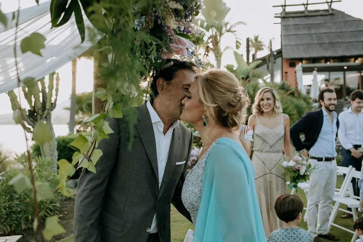 El novio recibe a la novia con un beso en la mejilla junto al arco