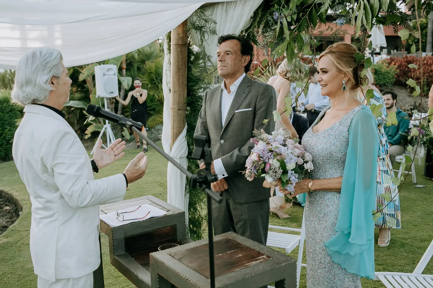 El oficiante, de traje blanco, habla a los novios ante el micrófono