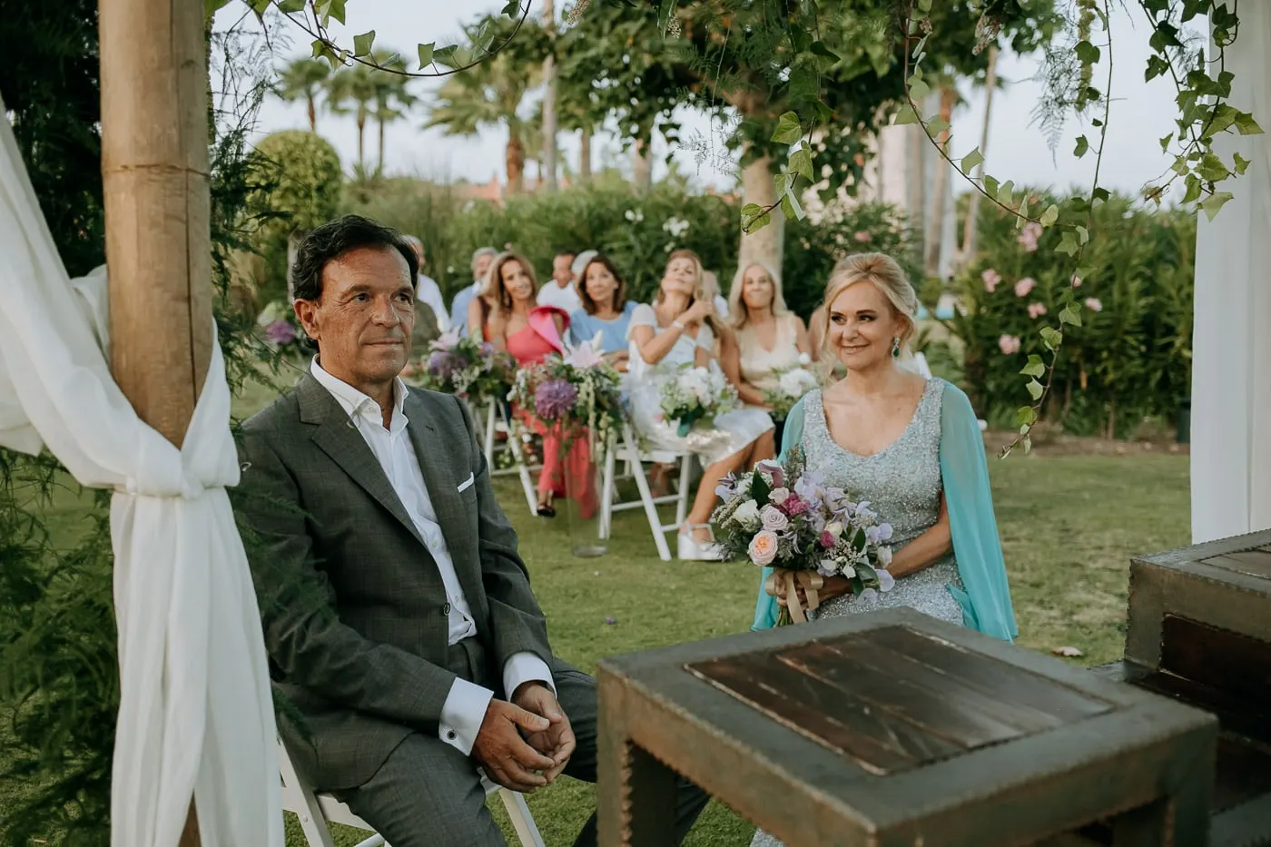 Los novios sentados en la ceremonia, con los invitados detrás