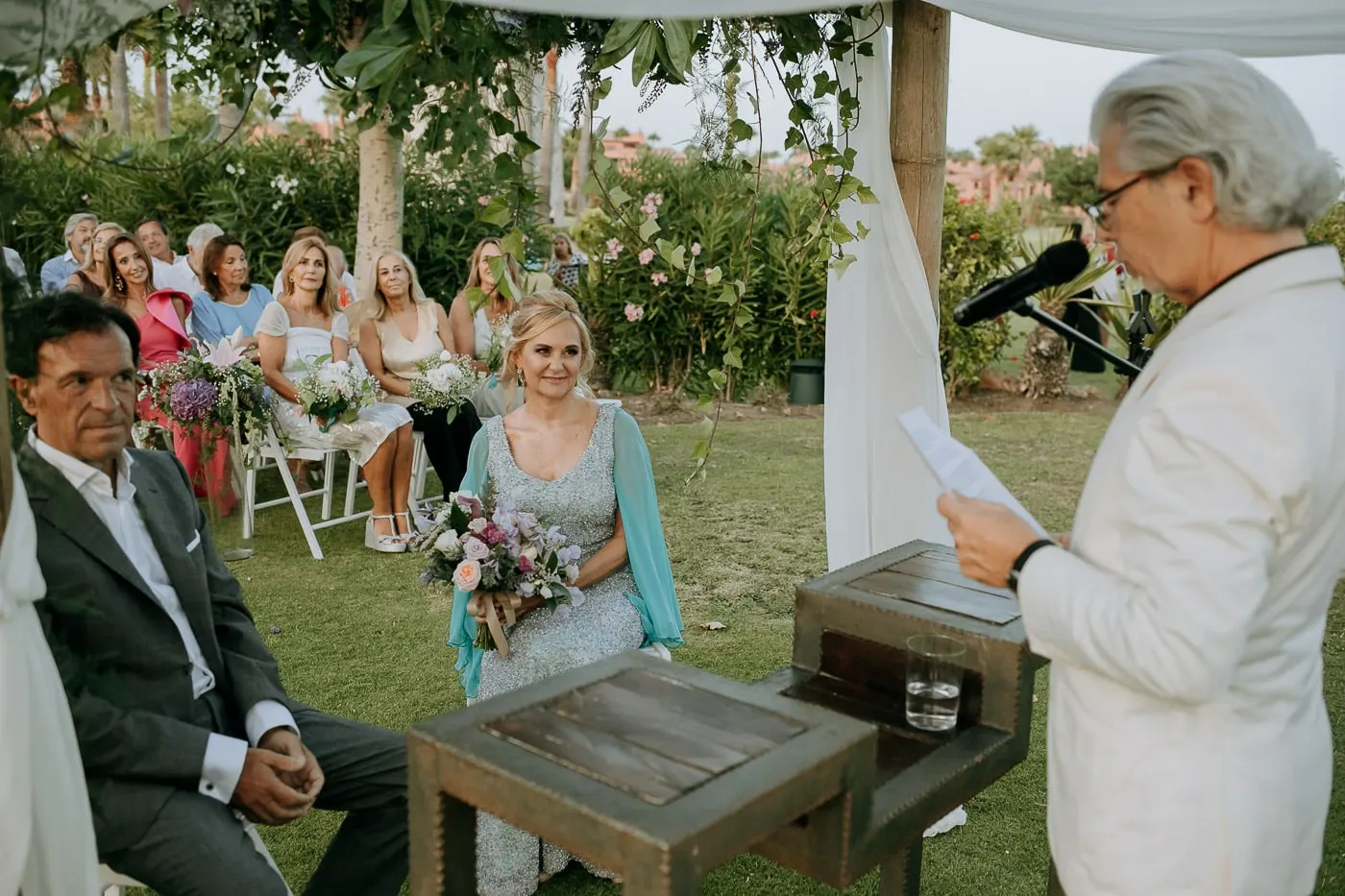 El oficiante de blanco lee mientras los novios escuchan