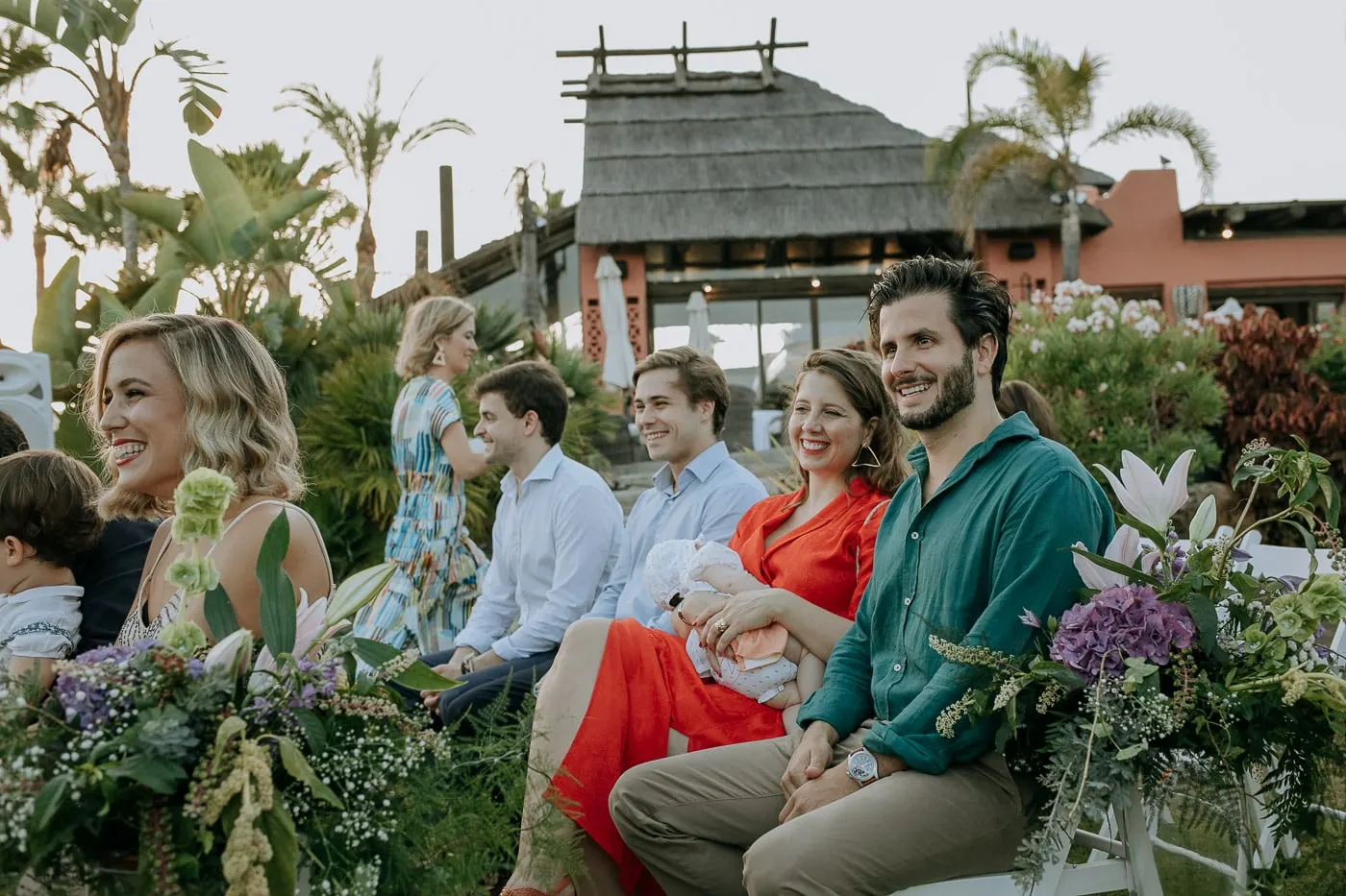 Invitados sentados en el jardín con el tejado de paja detrás