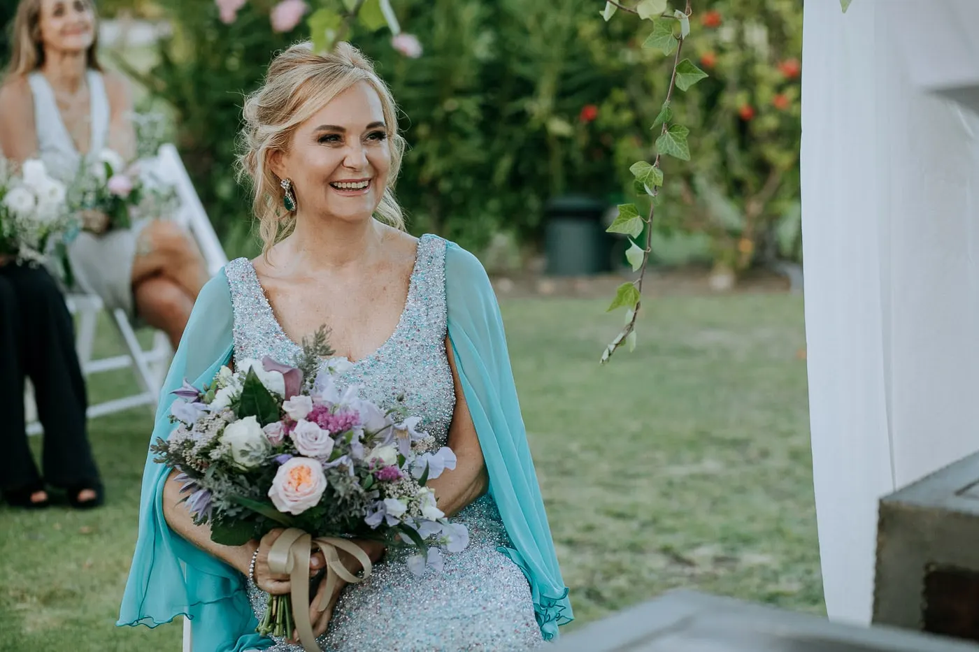 La novia se ríe en su silla, con el ramo en el regazo