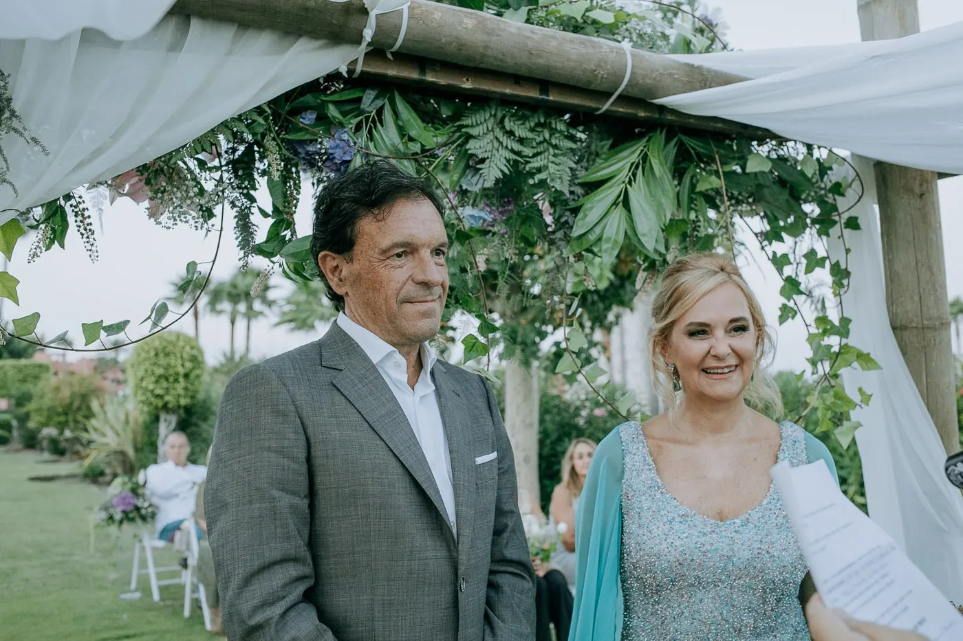 Los novios sonríen bajo el arco de hojas