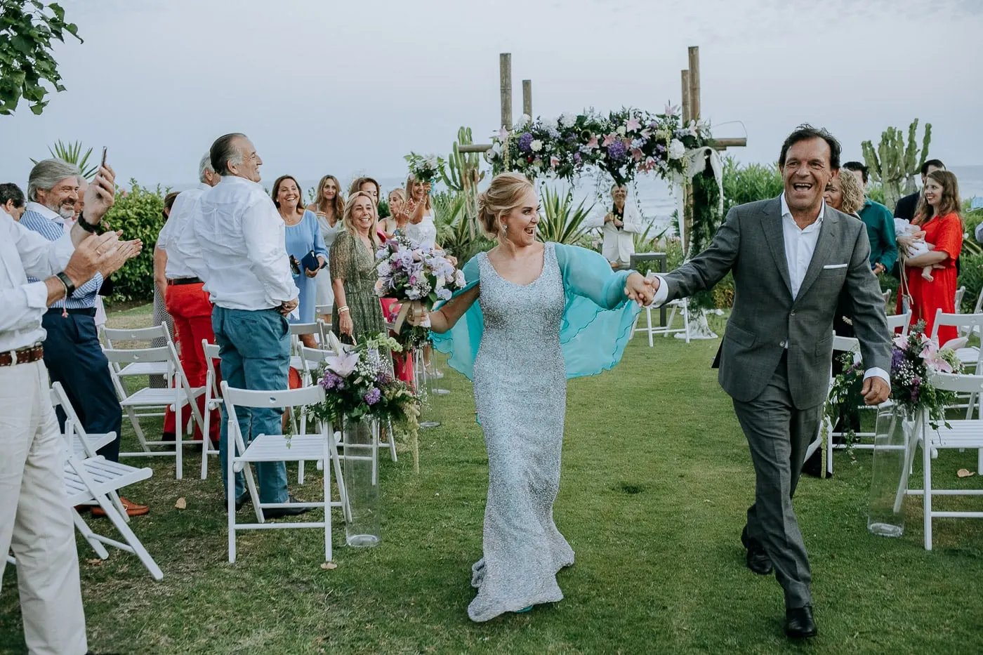 Los novios salen del brazo entre las sillas blancas