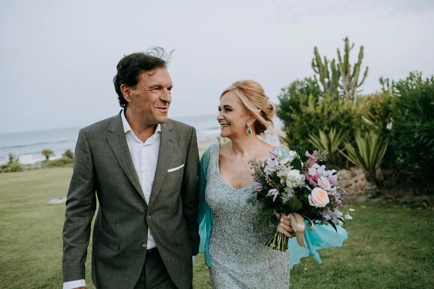 Los novios cruzan el césped con el mar detrás