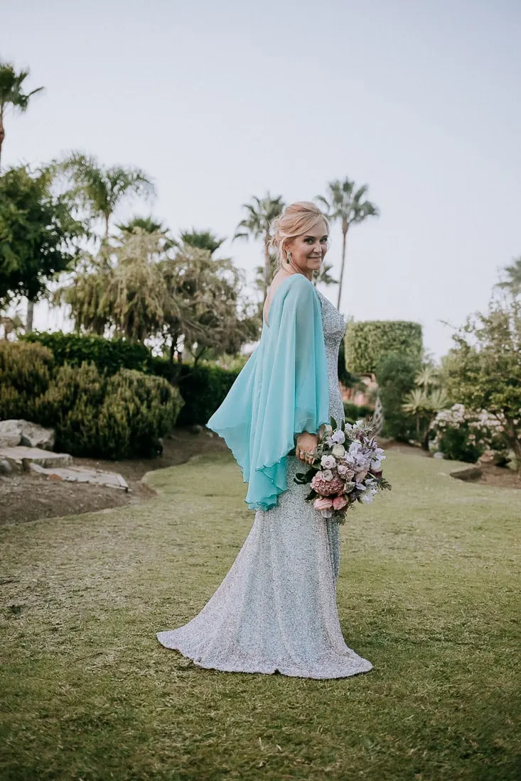 La novia con su vestido plateado y capa turquesa en el césped