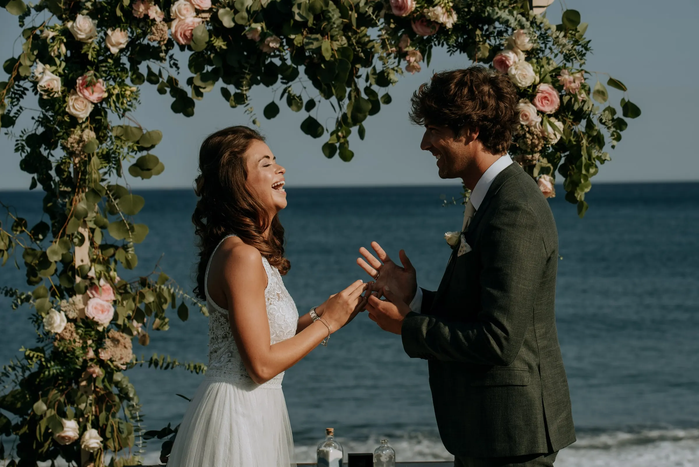 La novia se ríe mientras el novio le pone el anillo bajo el arco de flores, Trocadero, Sotogrande