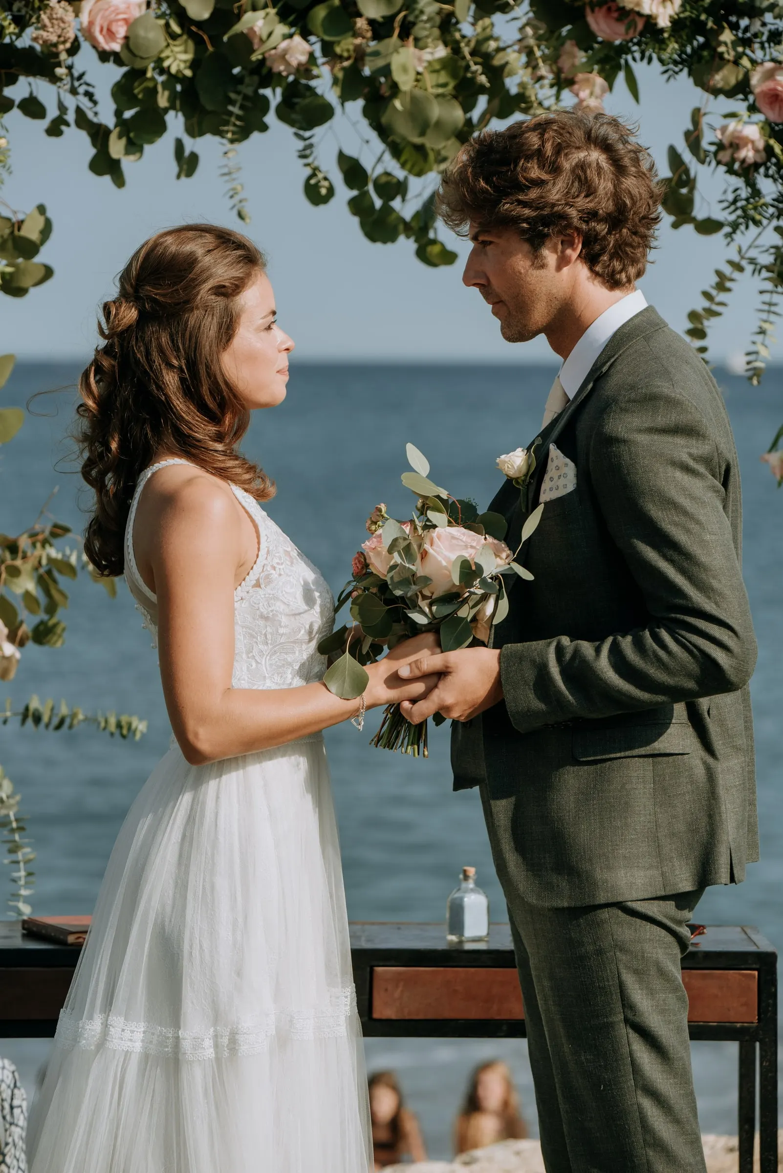 Los novios cogidos de las manos frente a la mesa de ceremonia y el mar, Trocadero, Sotogrande