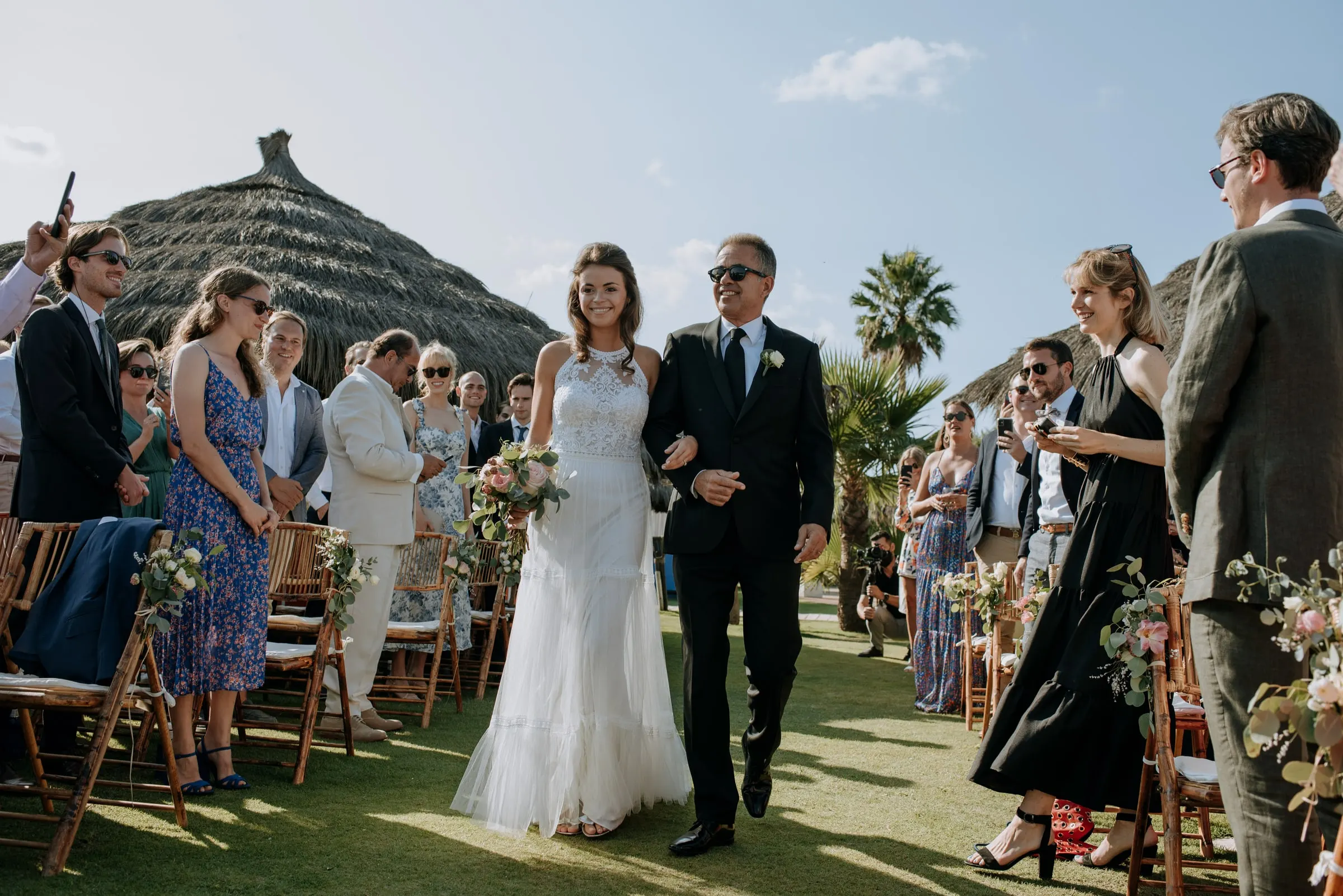 La novia avanza por el pasillo del brazo de su padre entre invitados sonrientes, Trocadero, Sotogrande
