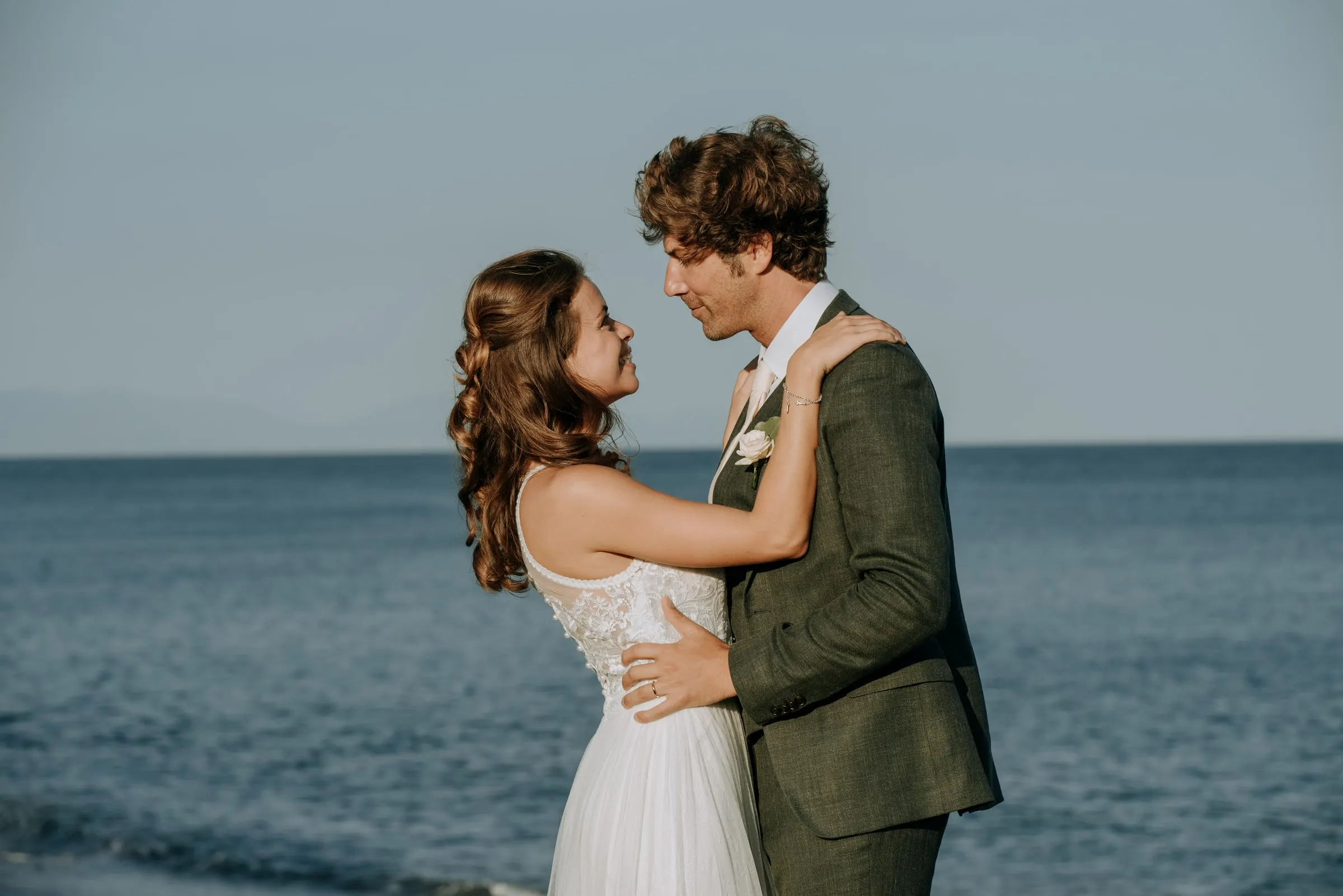 La novia abraza al novio por el cuello, los dos sonriendo, con el mar detrás, Trocadero, Sotogrande