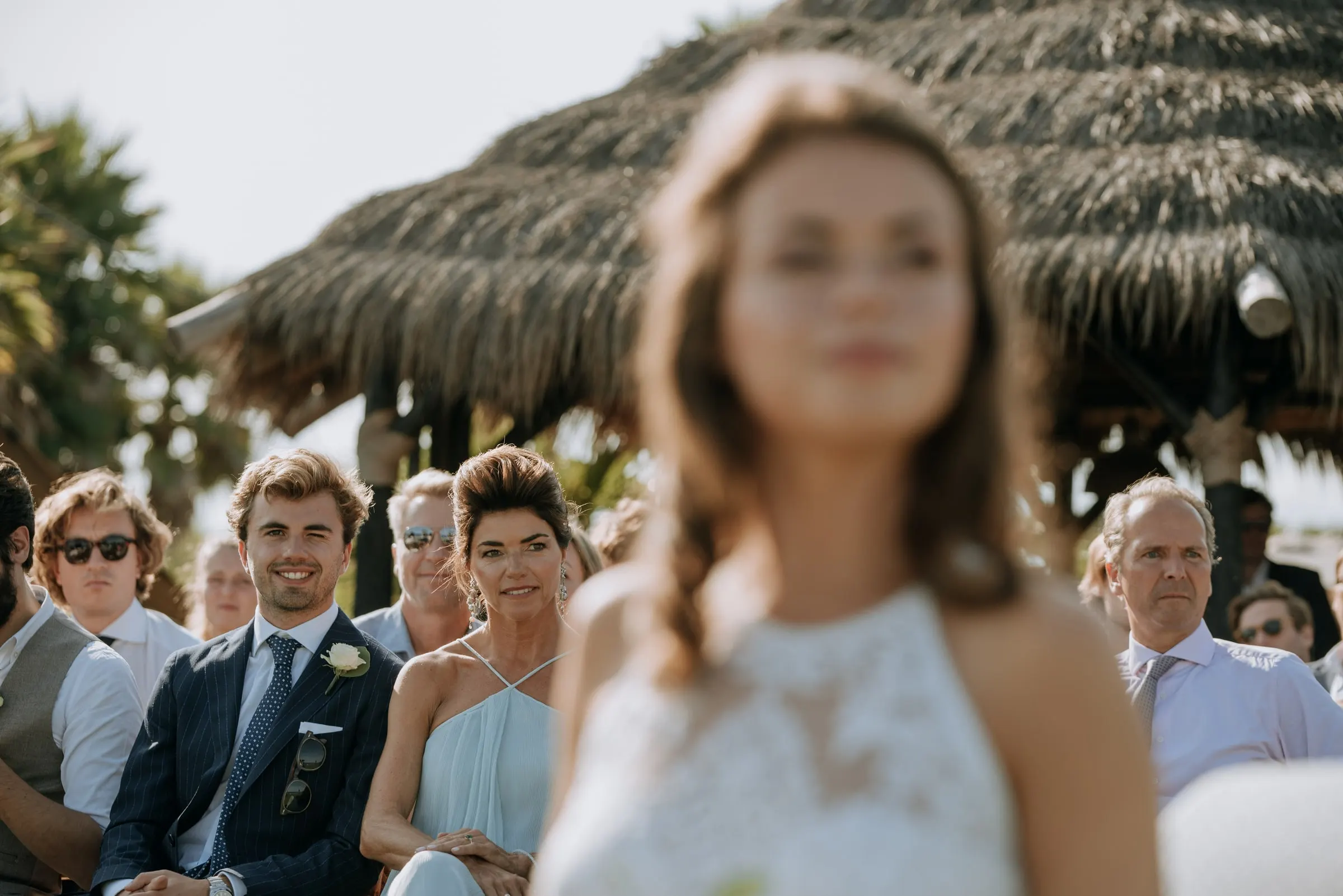 Invitados sonrientes en sus sillas mientras la novia pasa desenfocada en primer plano, Trocadero, Sotogrande
