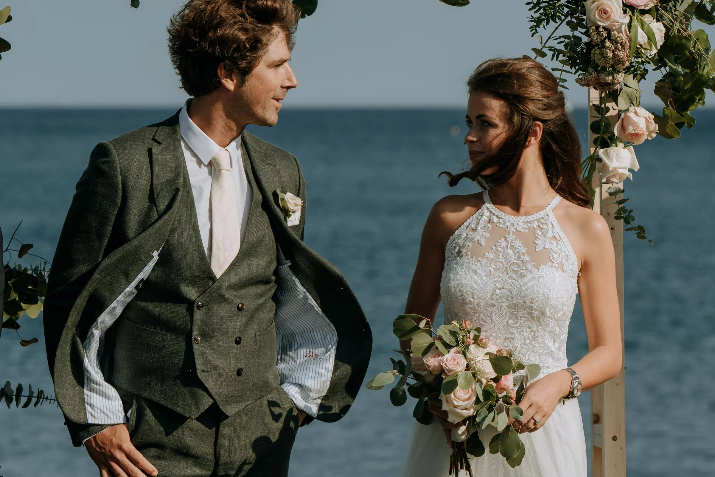 El novio con traje verde y la novia con el ramo miran hacia el mar, Trocadero, Sotogrande
