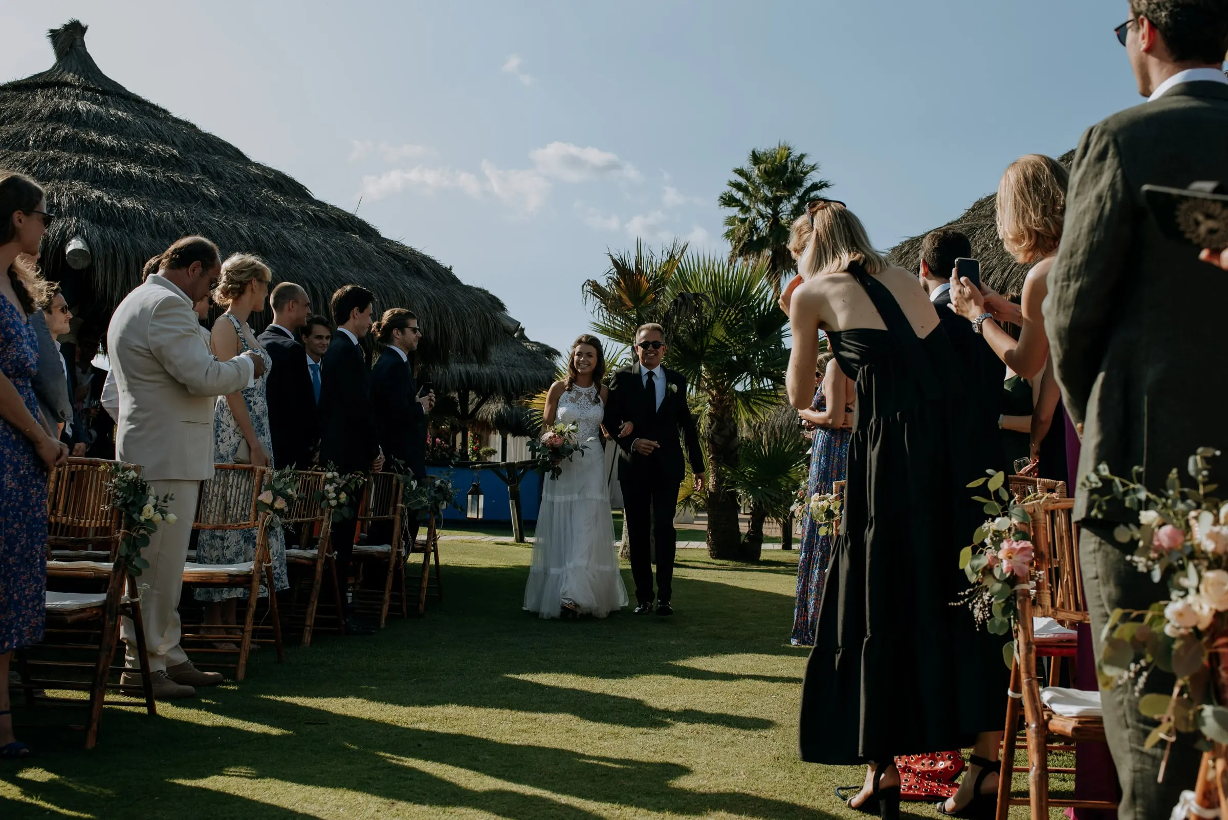 La novia y su padre recorren el pasillo de césped con los invitados en pie, Trocadero, Sotogrande