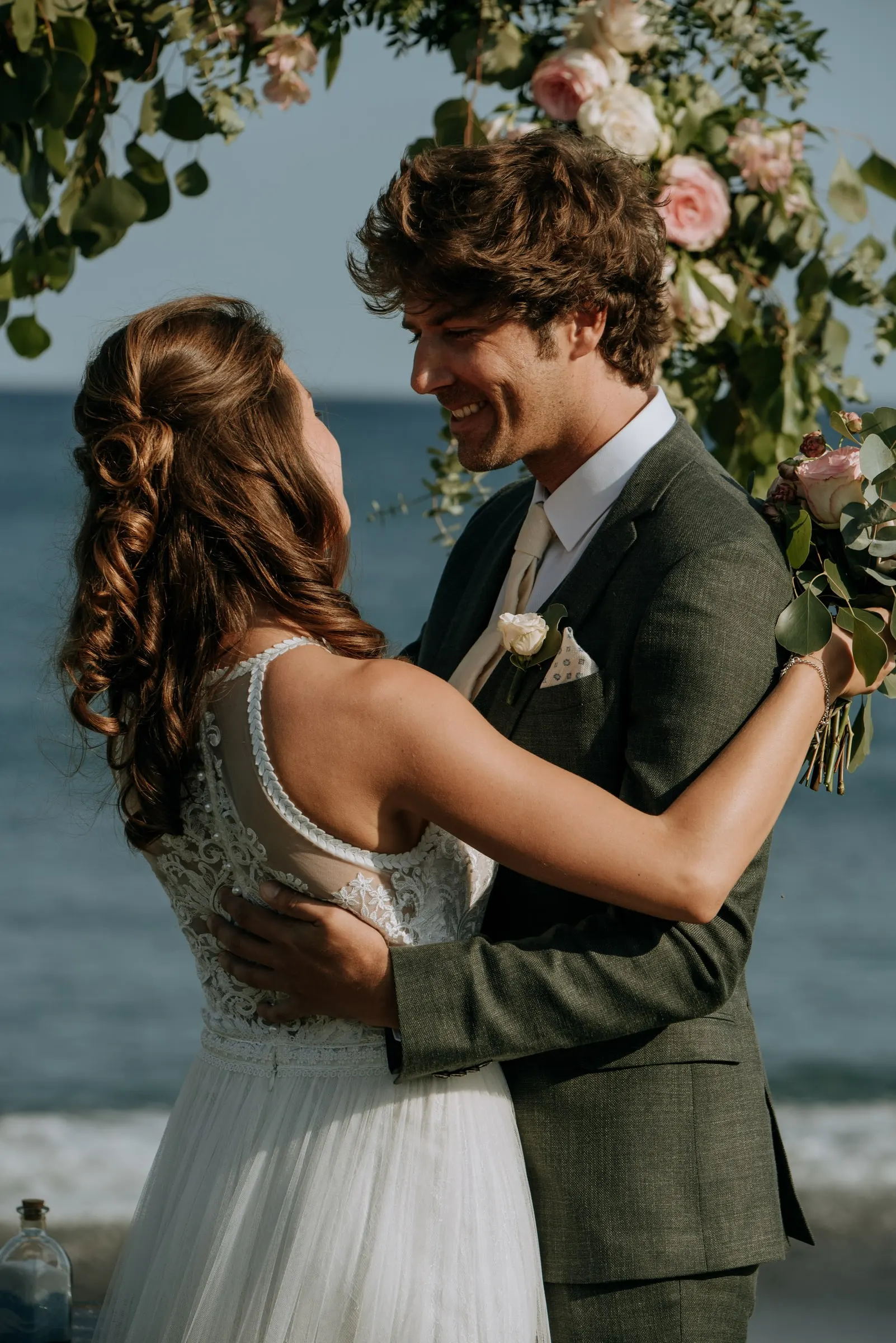 Los novios se abrazan sonrientes bajo el arco de flores junto al mar, Trocadero, Sotogrande