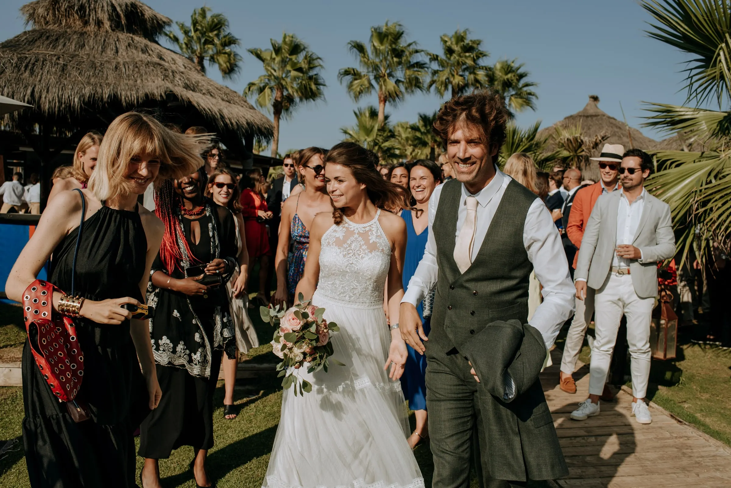 Los novios avanzan entre los invitados por un camino flanqueado de palmeras, Trocadero, Sotogrande