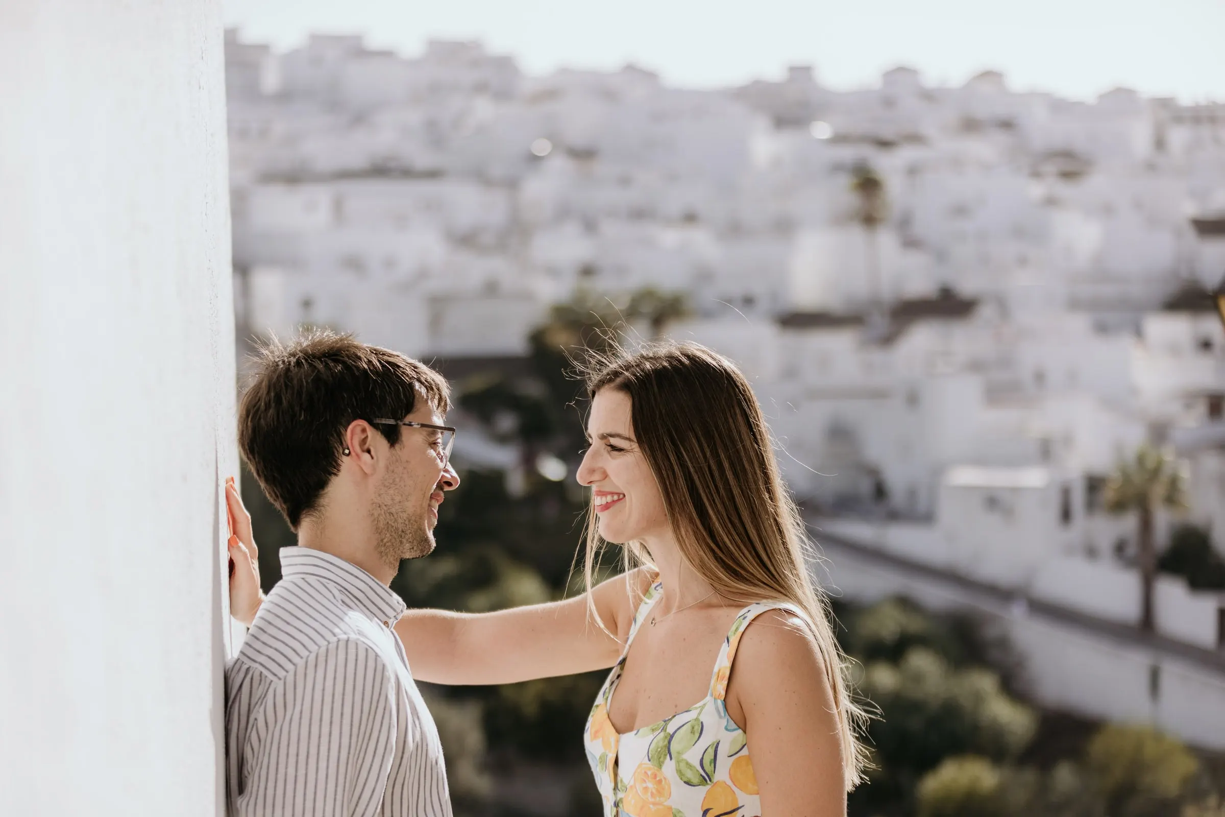 La pareja ríe junto a una pared blanca con el pueblo encalado de Vejer desenfocado detrás