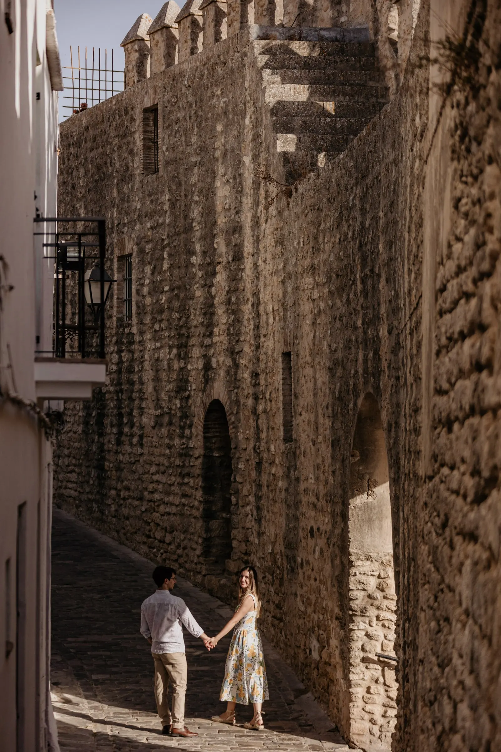 La pareja pasea de la mano por una calle medieval estrecha junto a la muralla de Vejer