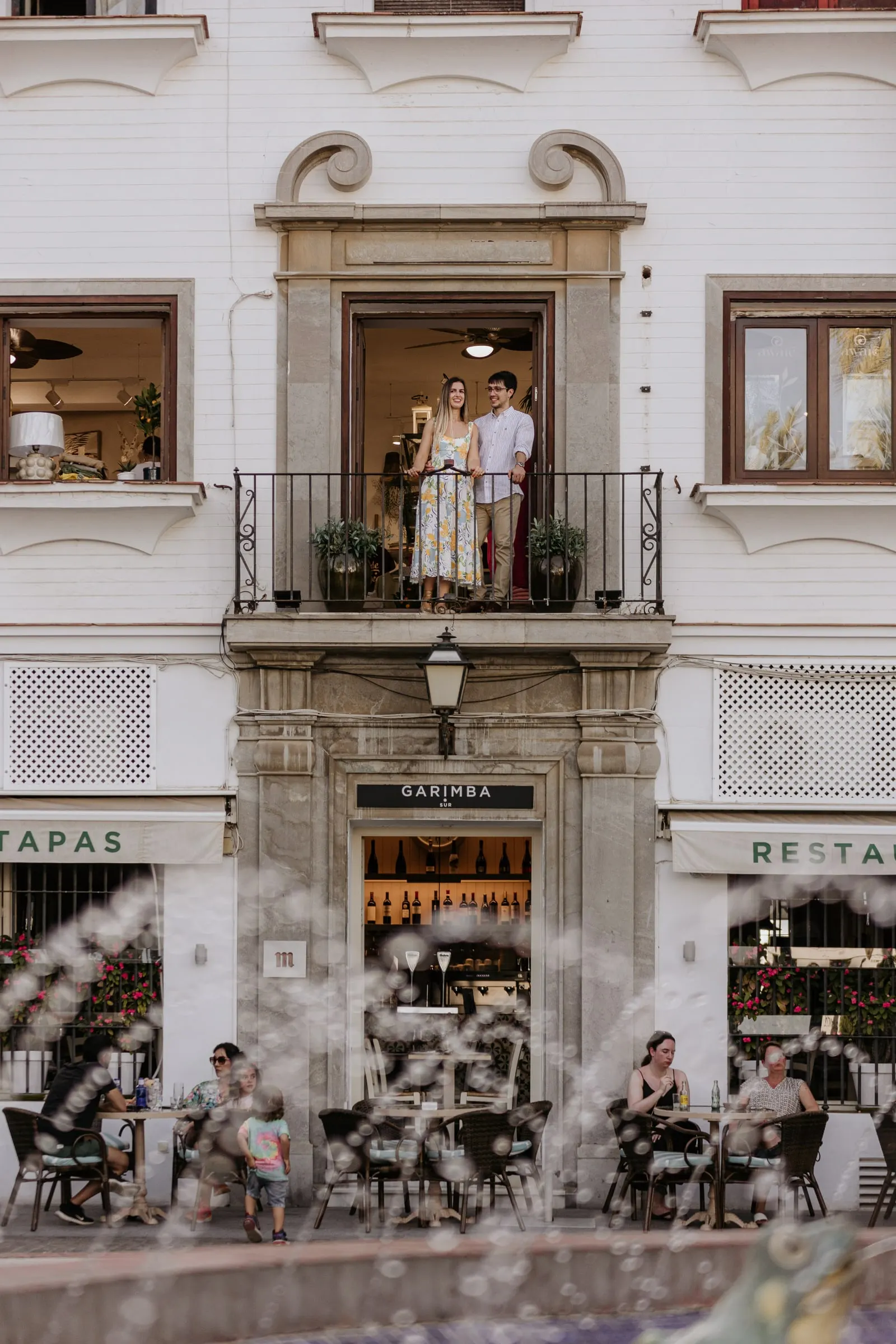 La pareja en el balcón de un edificio blanco sobre las terrazas de la Plaza de España de Vejer