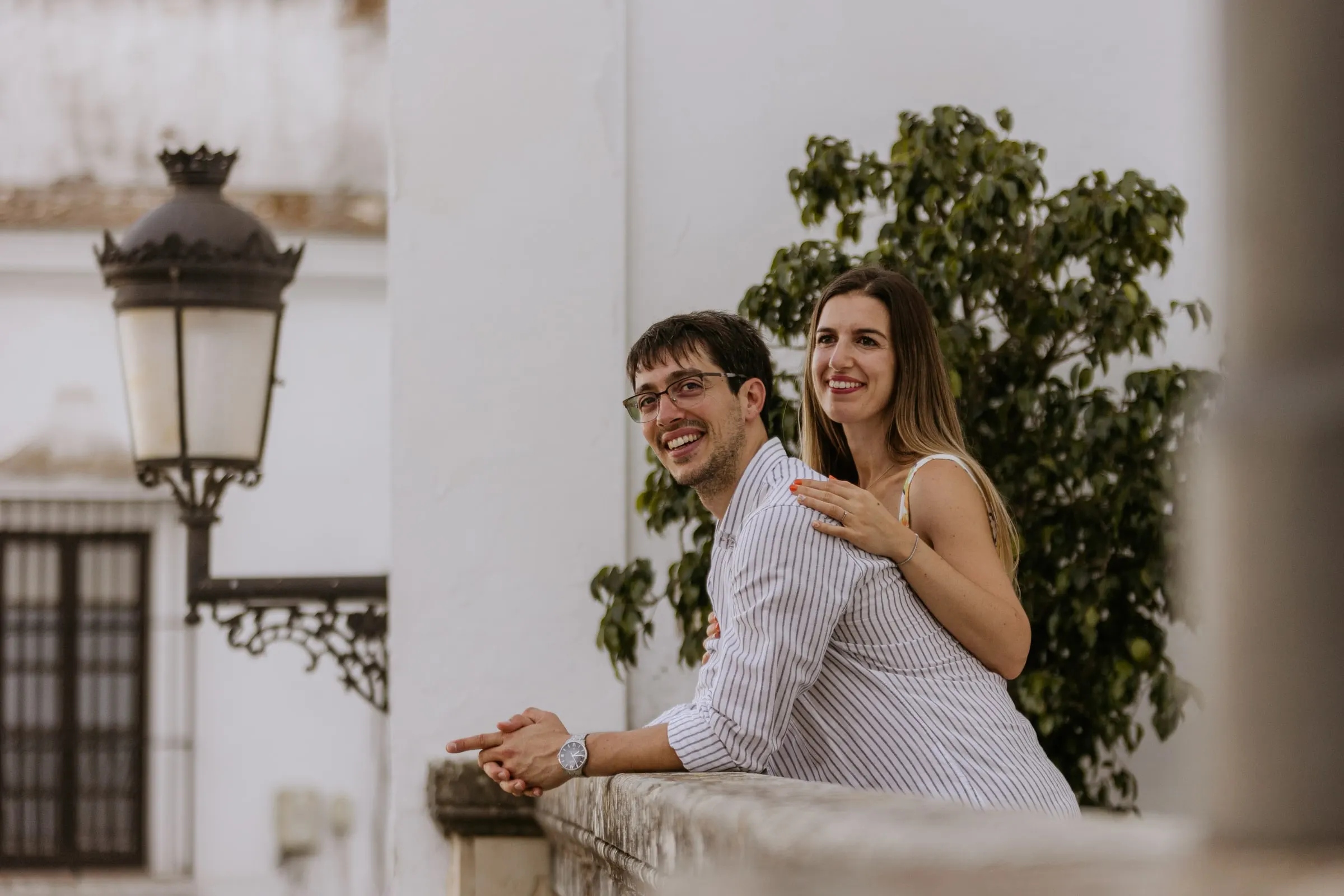 La pareja apoyada en un muro junto a una farola antigua y una higuera en Vejer