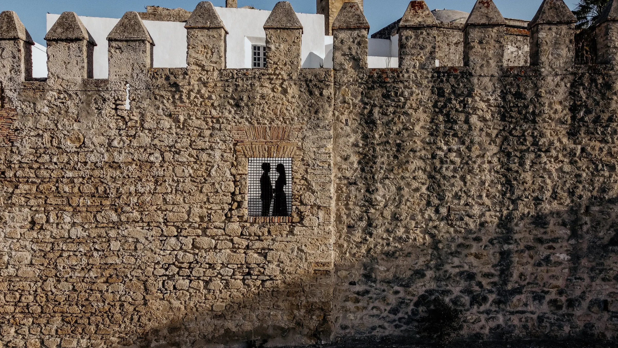 La pareja enmarcada en un ventanuco de la muralla almenada del castillo de Vejer de la Frontera