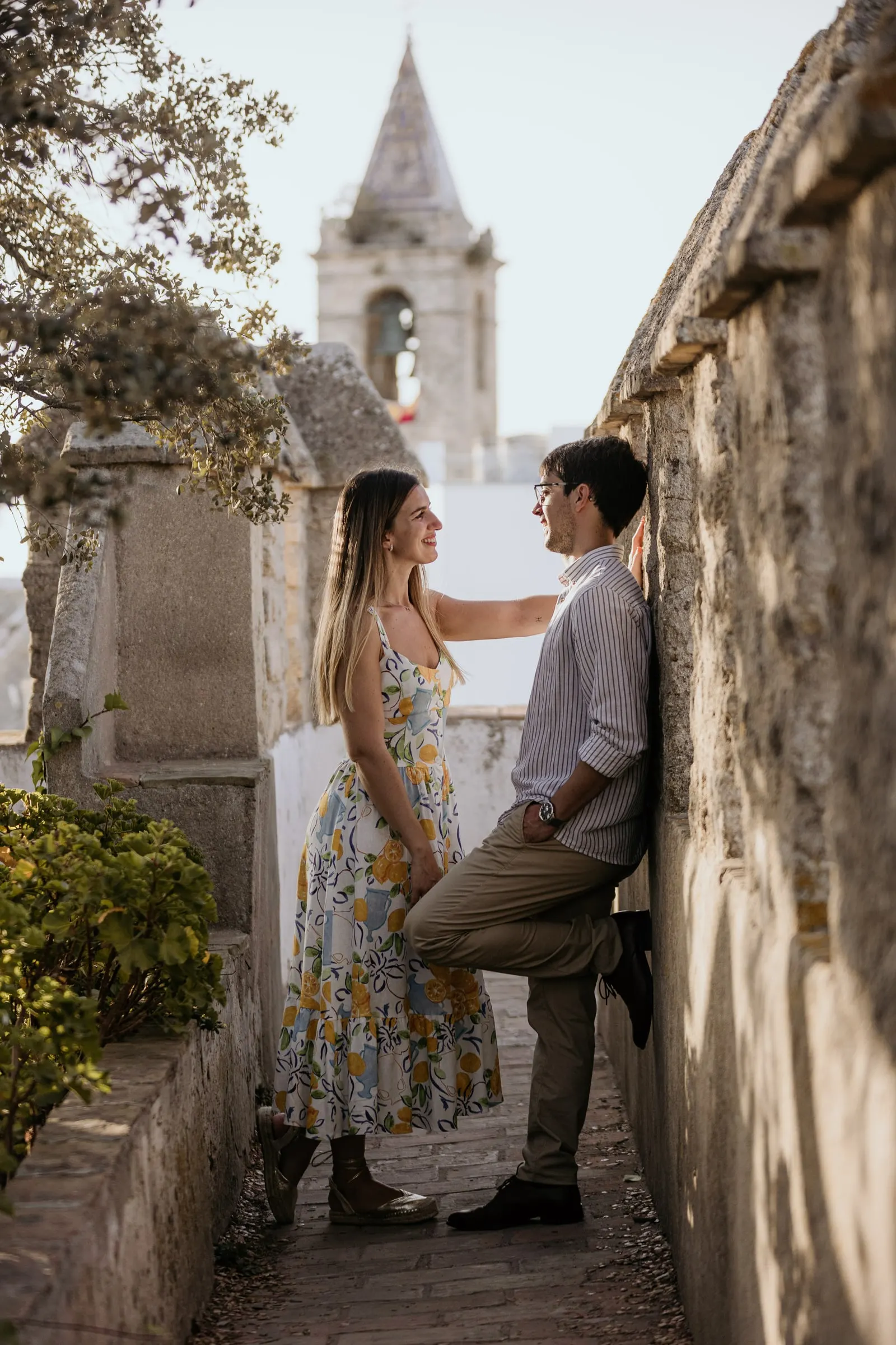 La pareja junto a un viejo muro de piedra bajo el campanario de una iglesia en Vejer de la Frontera