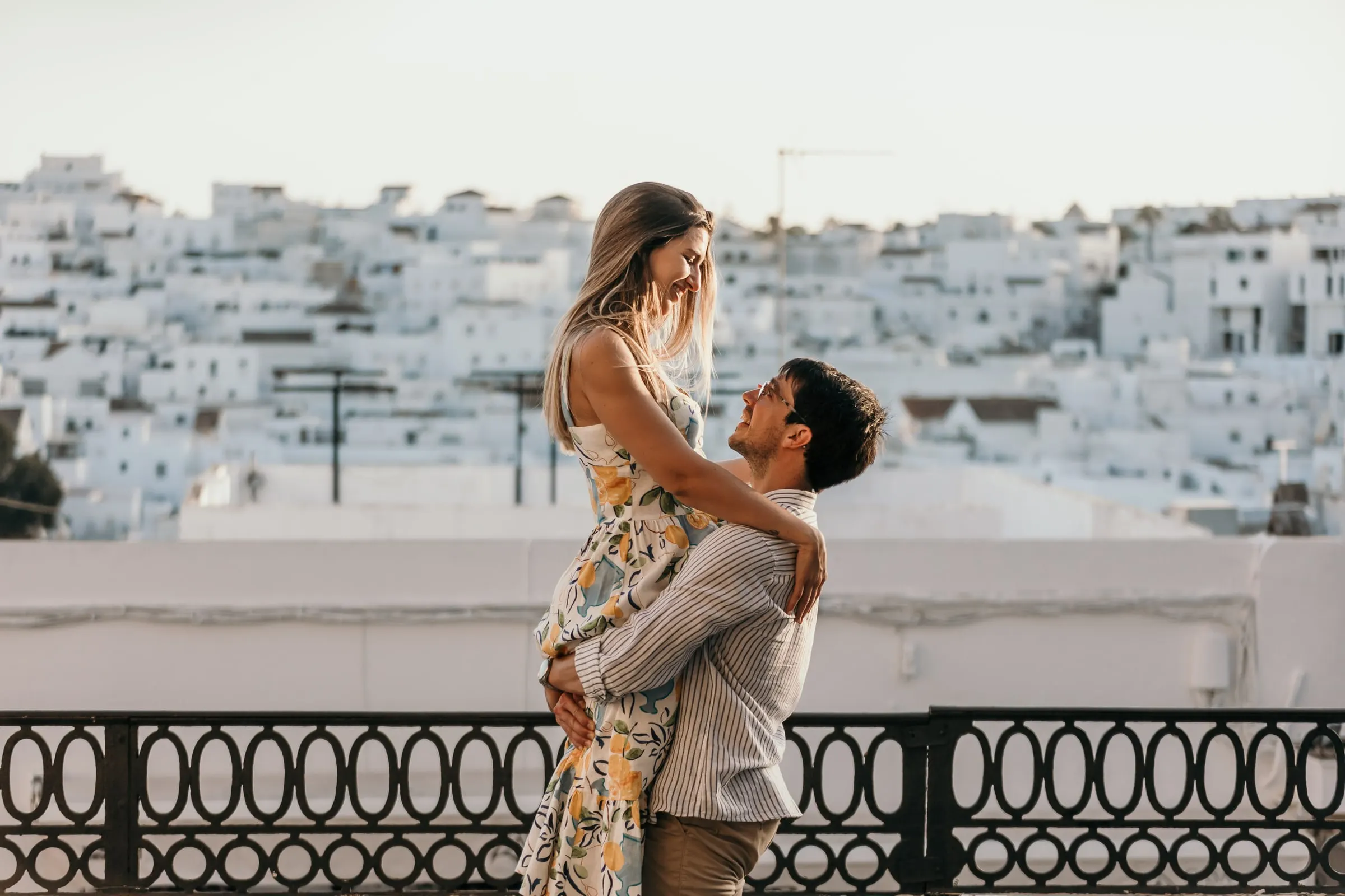 El prometido levanta a la futura novia junto a una baranda de hierro sobre el pueblo blanco de Vejer