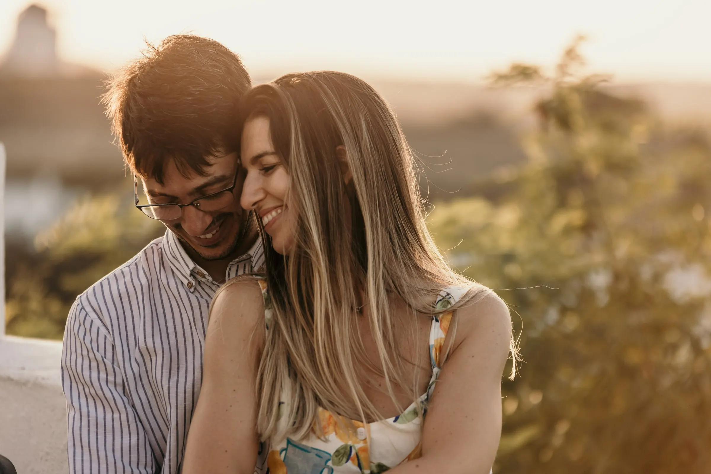La pareja mejilla con mejilla, ojos cerrados y sonriendo, con la luz cálida del atardecer en Andalucía