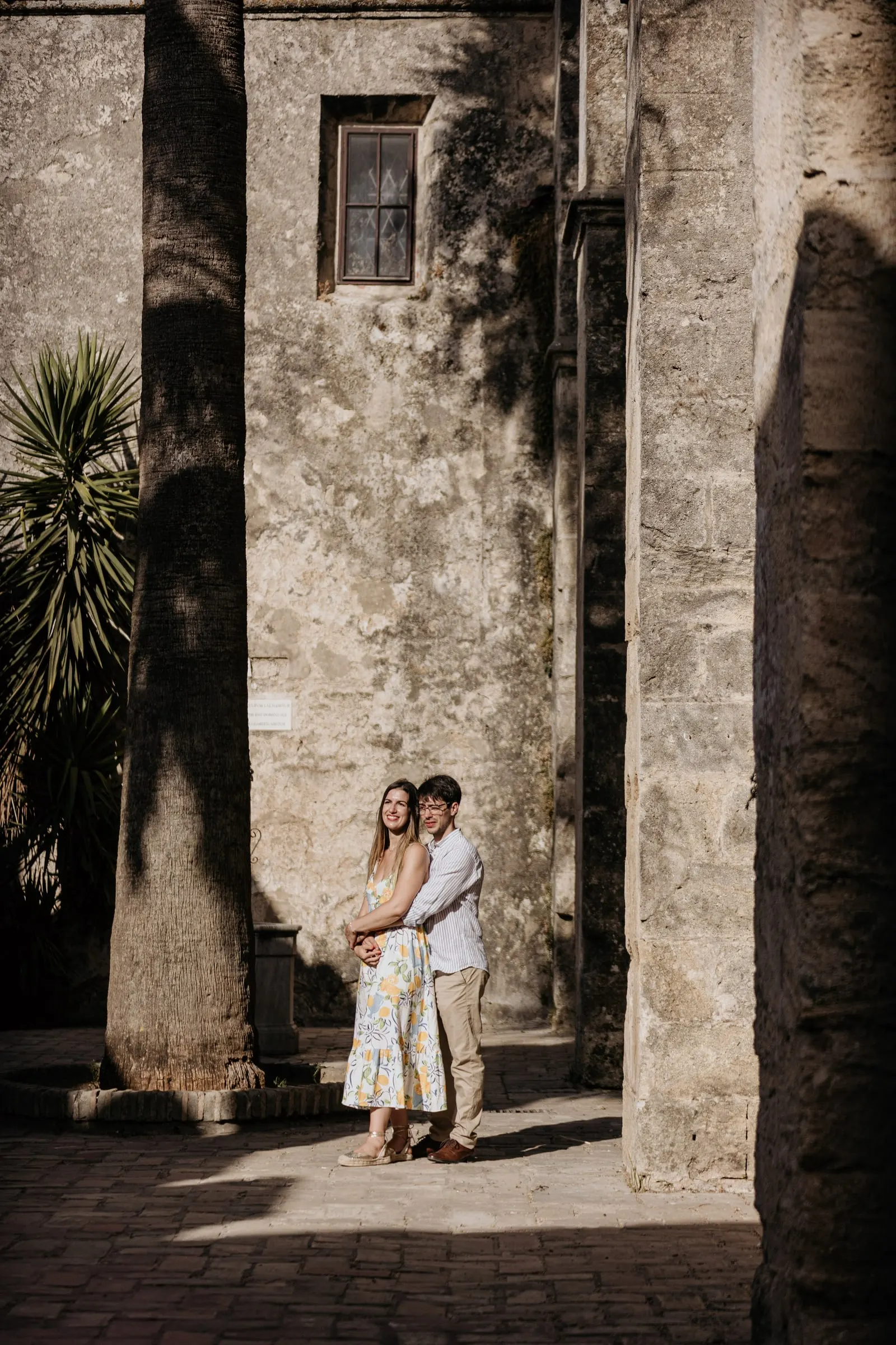 La pareja abrazada, pequeña entre altos muros de piedra y palmeras, en el casco antiguo de Vejer de la Frontera