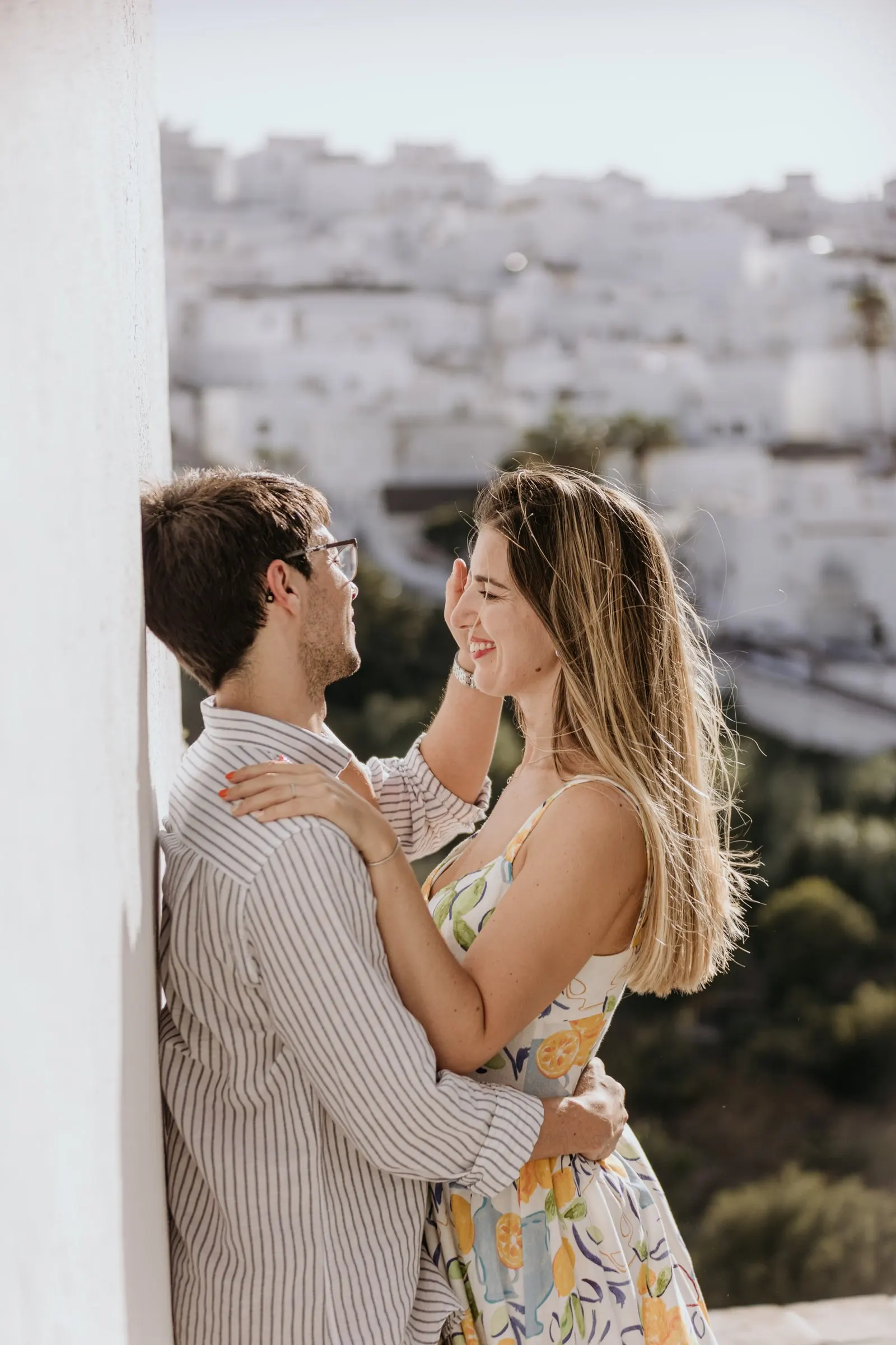 La pareja abrazada contra una pared blanca con la ladera encalada de Vejer desenfocada detrás