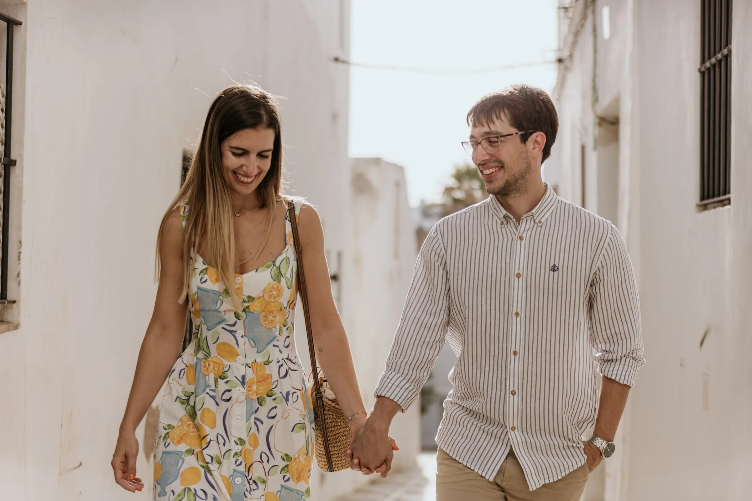 La pareja ríe mientras baja de la mano una calle blanca y soleada de Vejer de la Frontera