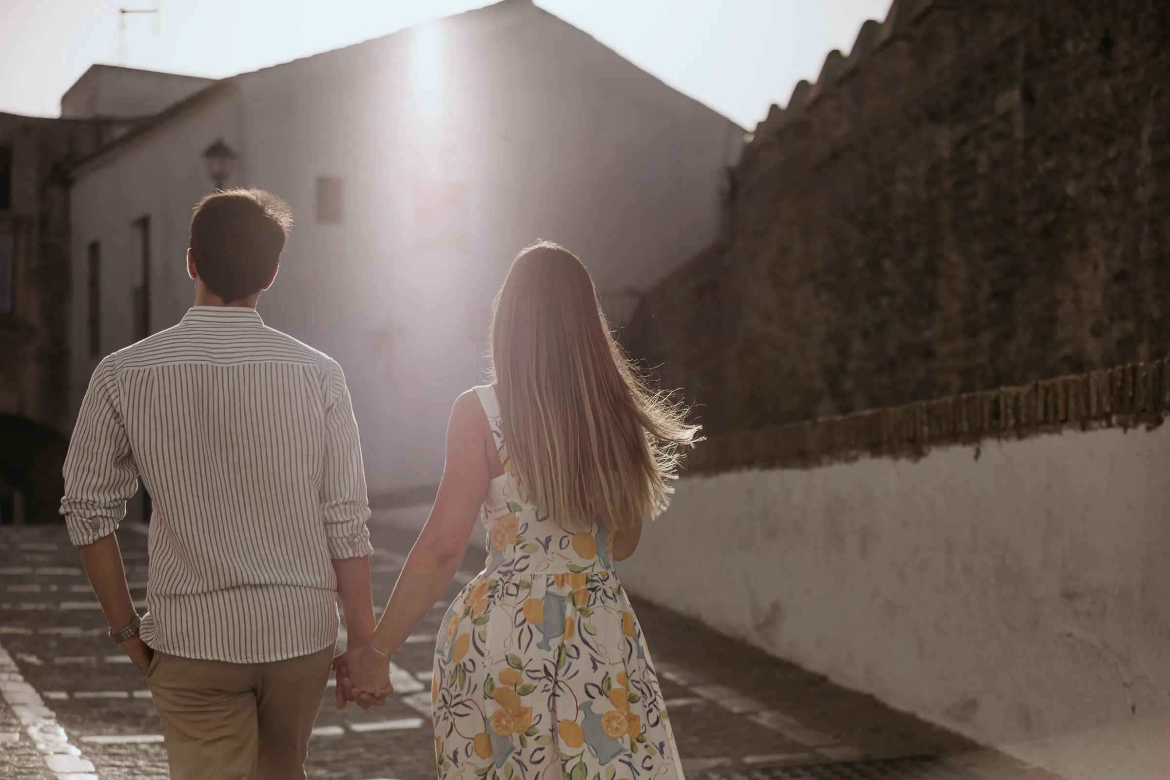 La pareja de espaldas camina de la mano junto a la muralla hacia la luz, Vejer