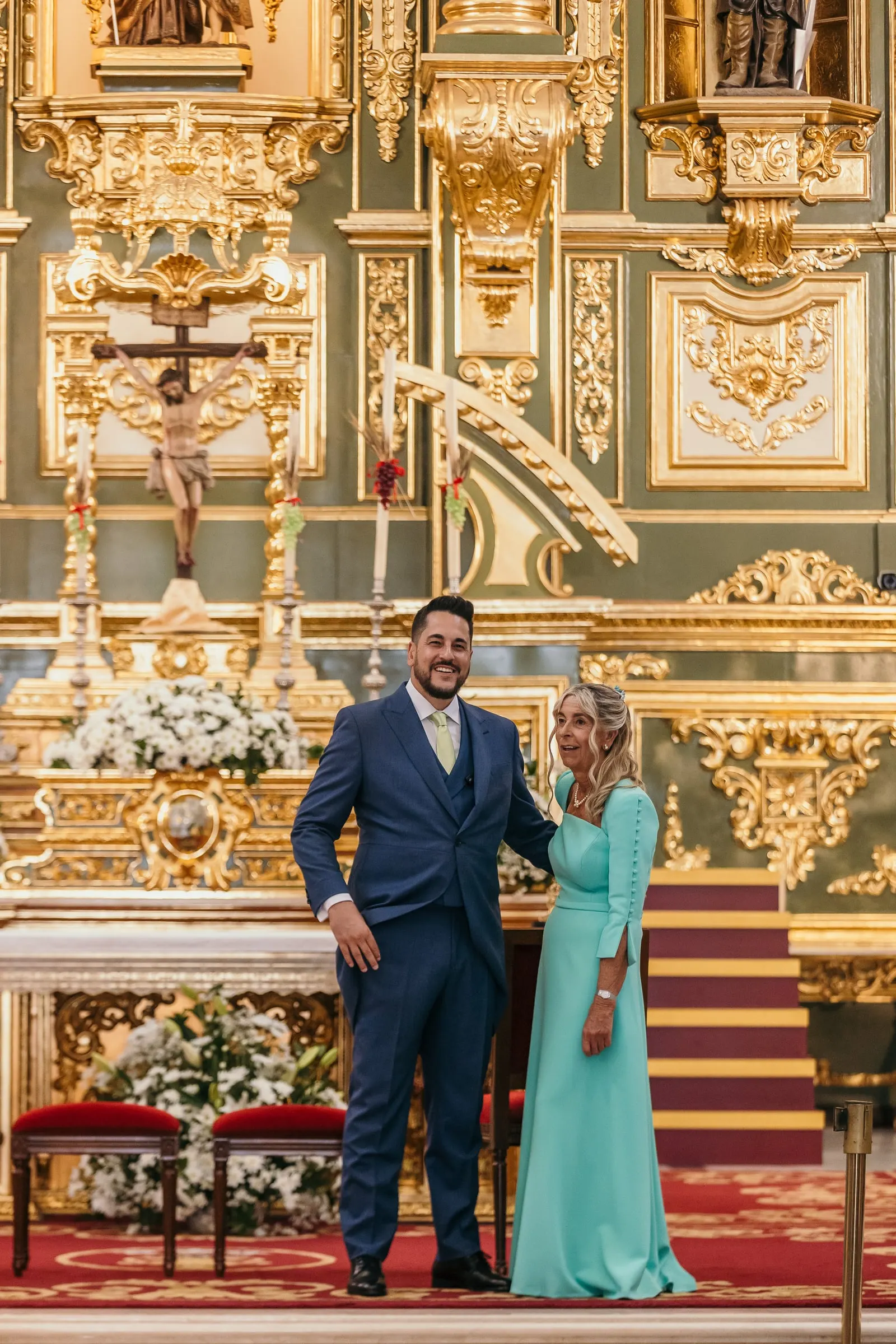 El novio y su madre esperan en el altar ante el retablo dorado y verde