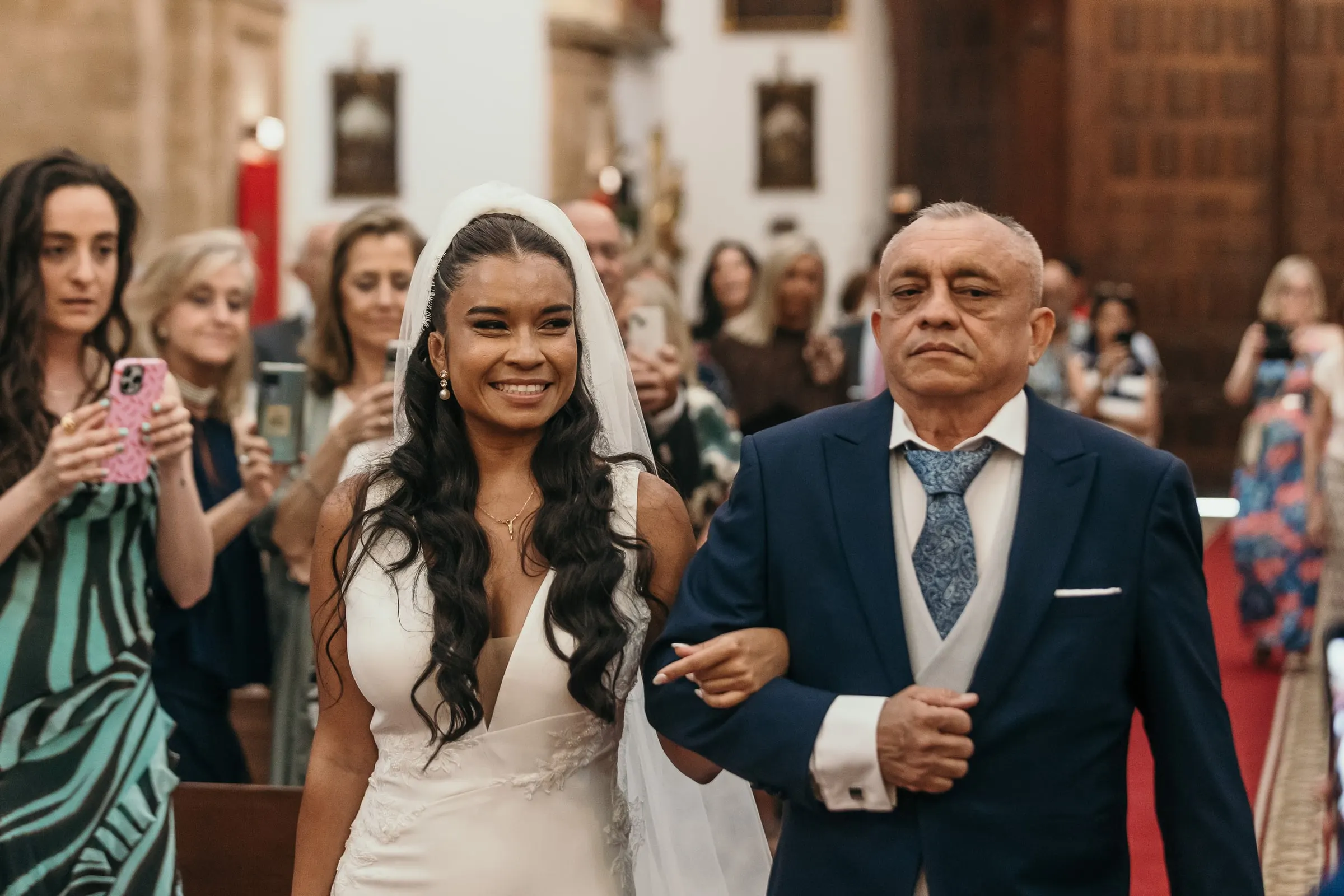 La novia sonríe a su padre mientras recorren el pasillo entre los invitados