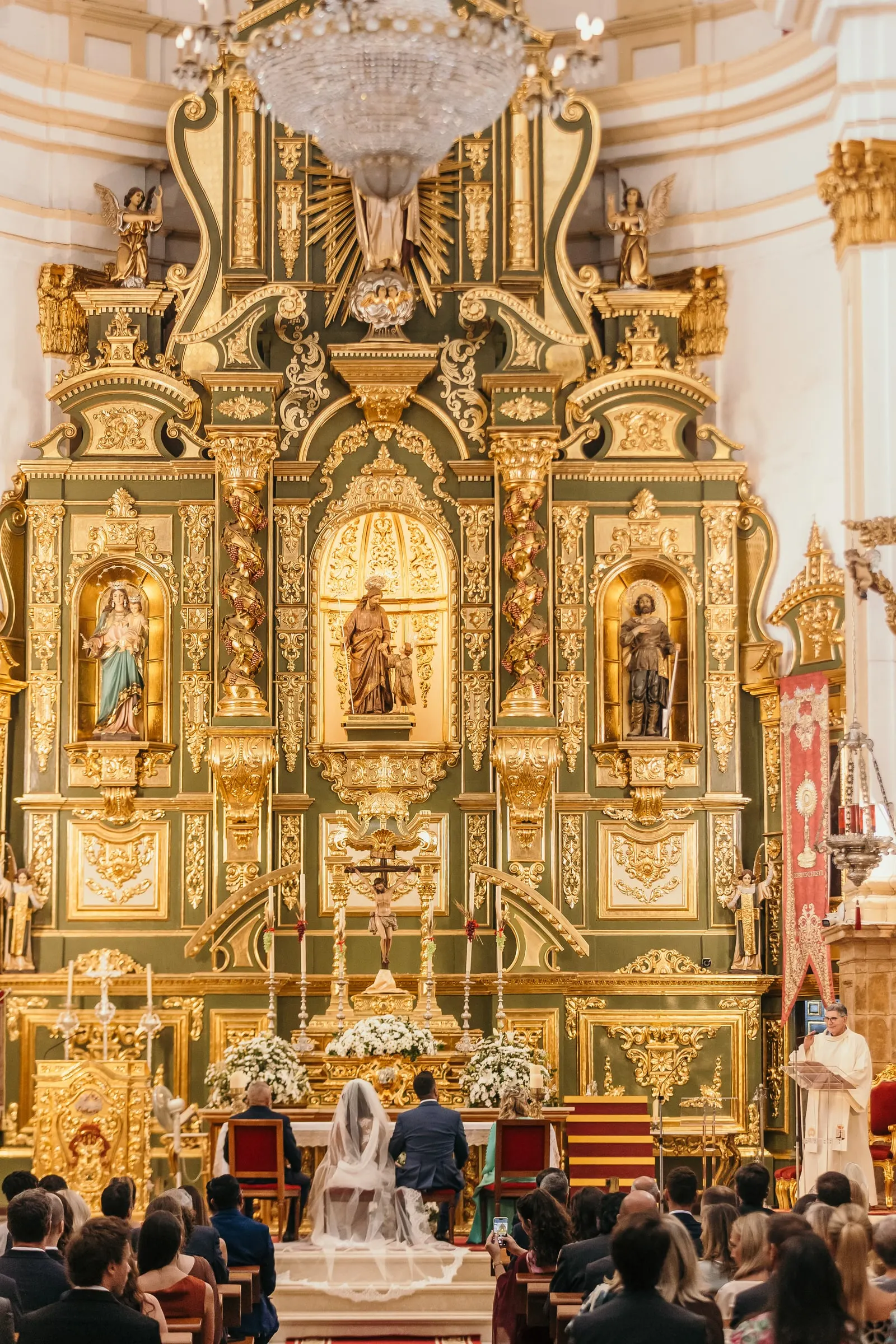 Vista general del retablo barroco dorado con los novios en el altar durante la ceremonia en Marbella