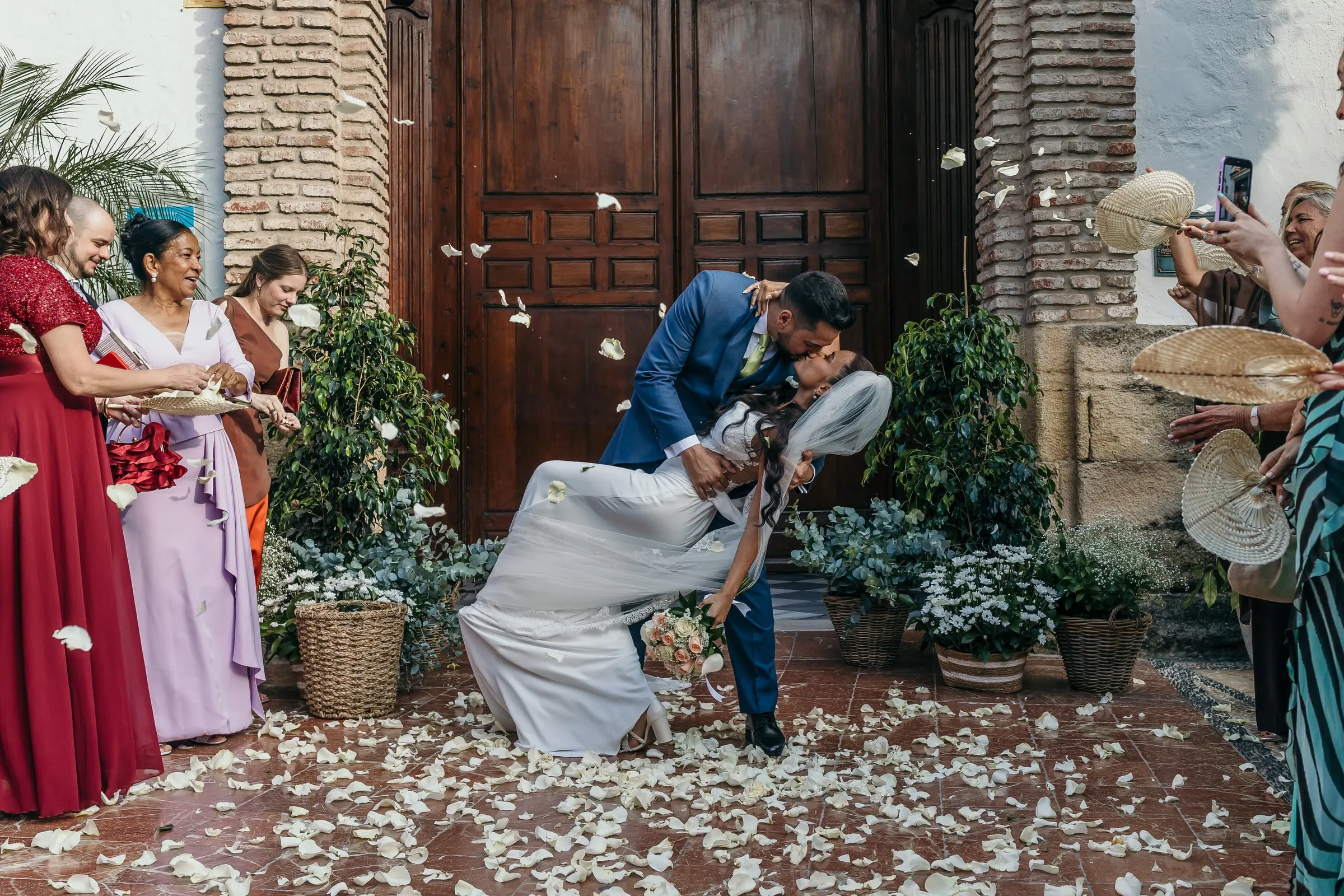 El novio inclina a la novia para besarla en la entrada de la iglesia cubierta de pétalos