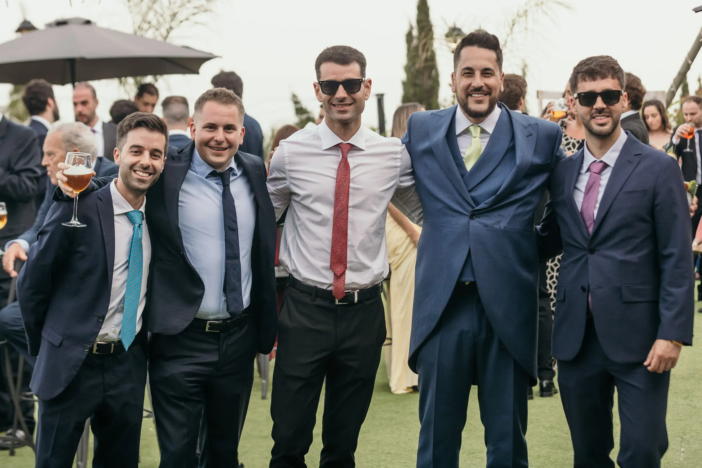 El novio con sus amigos, algunos con gafas de sol, posando en el césped durante el cóctel