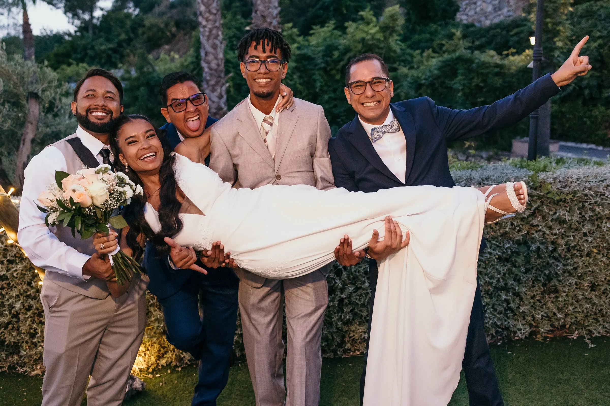 Los amigos de los novios cogen a la novia en brazos en el jardín al atardecer