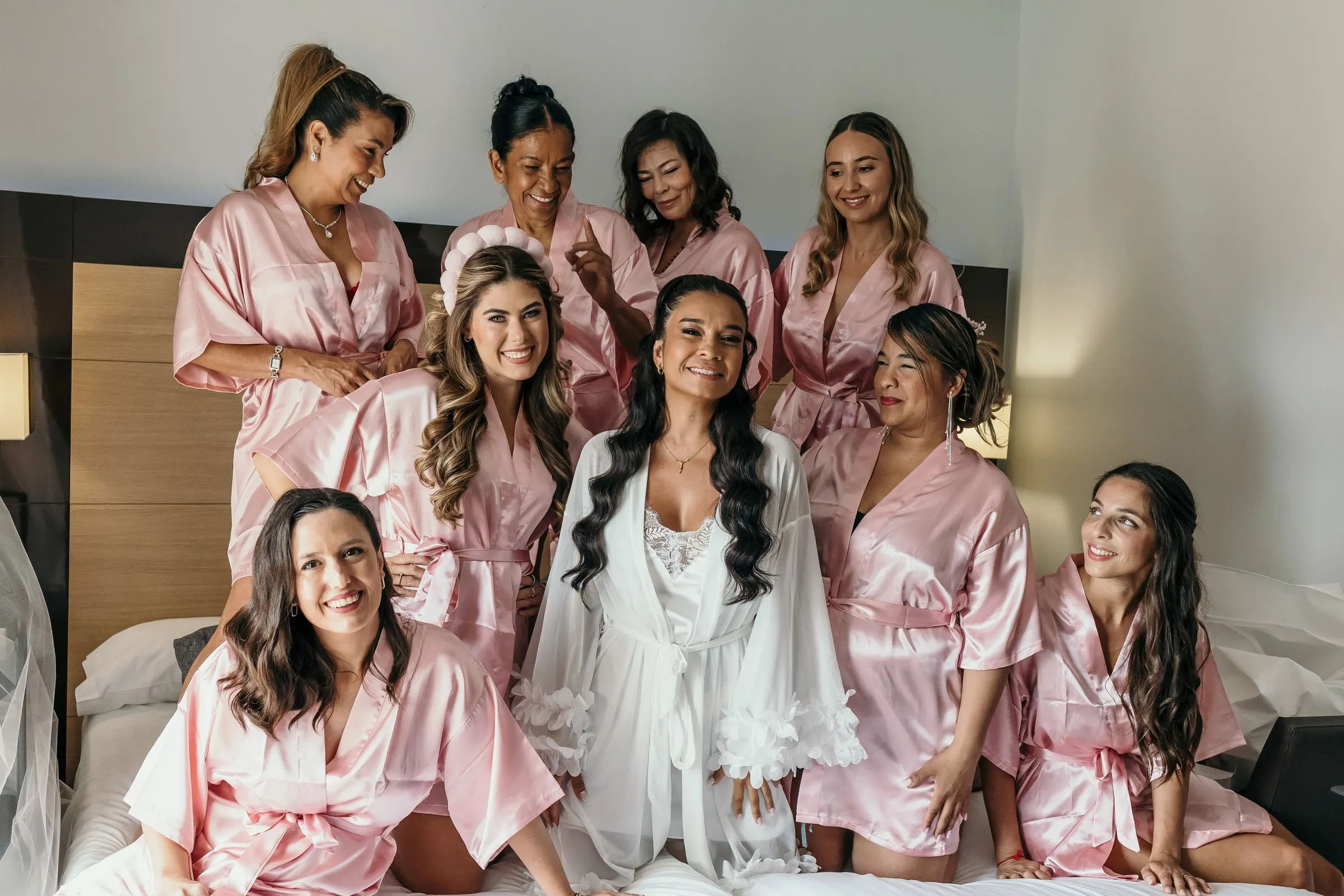 La novia en bata blanca sentada en la cama entre sus damas con batas de satén rosa, durante los preparativos en Marbella