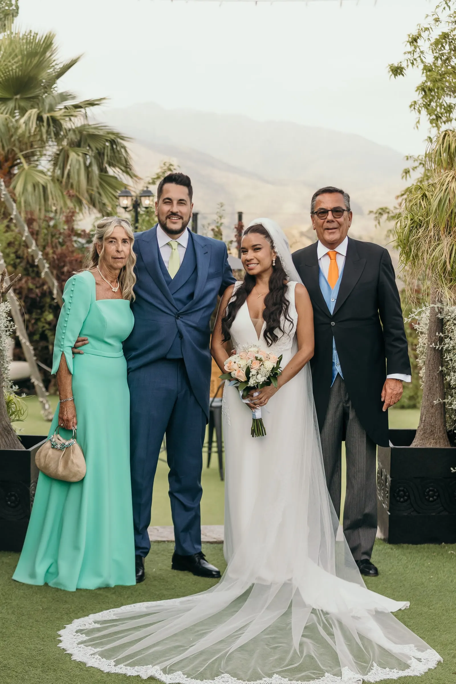Los novios con los padres del novio en el césped bajo las palmeras, con las colinas de Marbella detrás